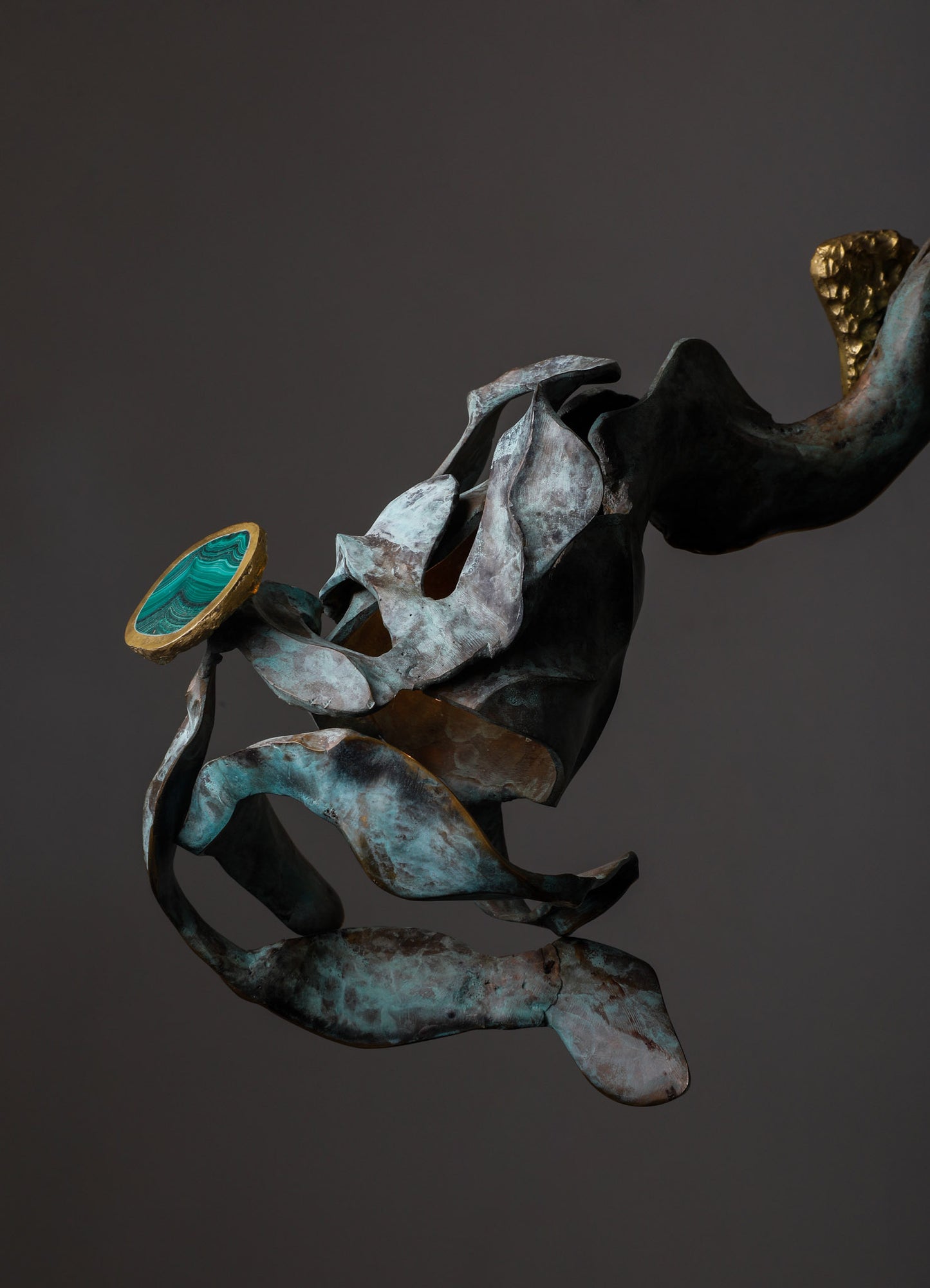 A modern abstract sculpture made of oxidized metal with flowing, organic shapes and a textured surface, accented with gold and turquoise elements. The piece has a contemporary, artistic style with contrasting metallic tones and smooth, rounded details.