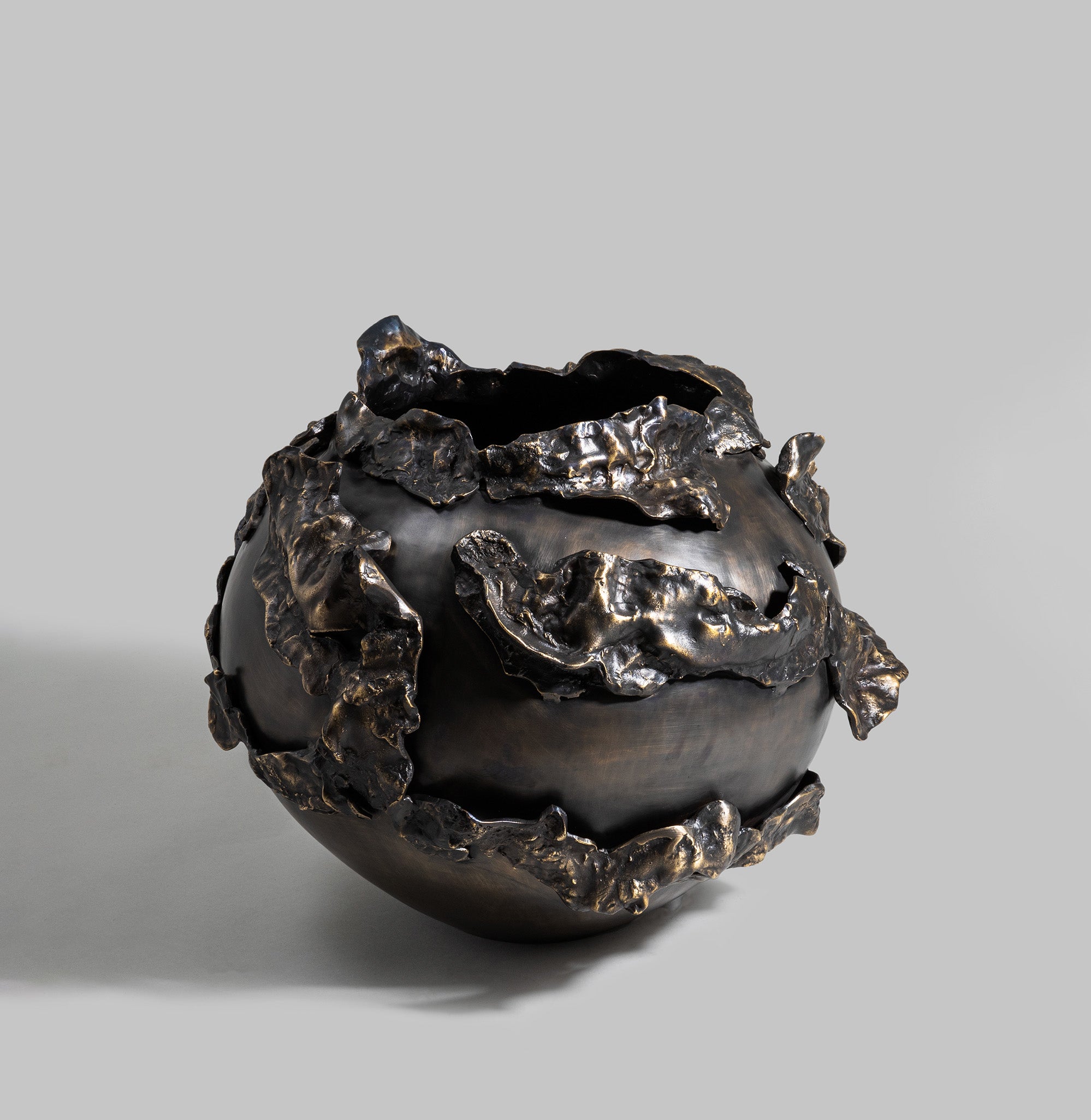 Black ceramic vase with irregular, textured metallic bronze accents and an organic, sculptural form, set against a plain gray background.