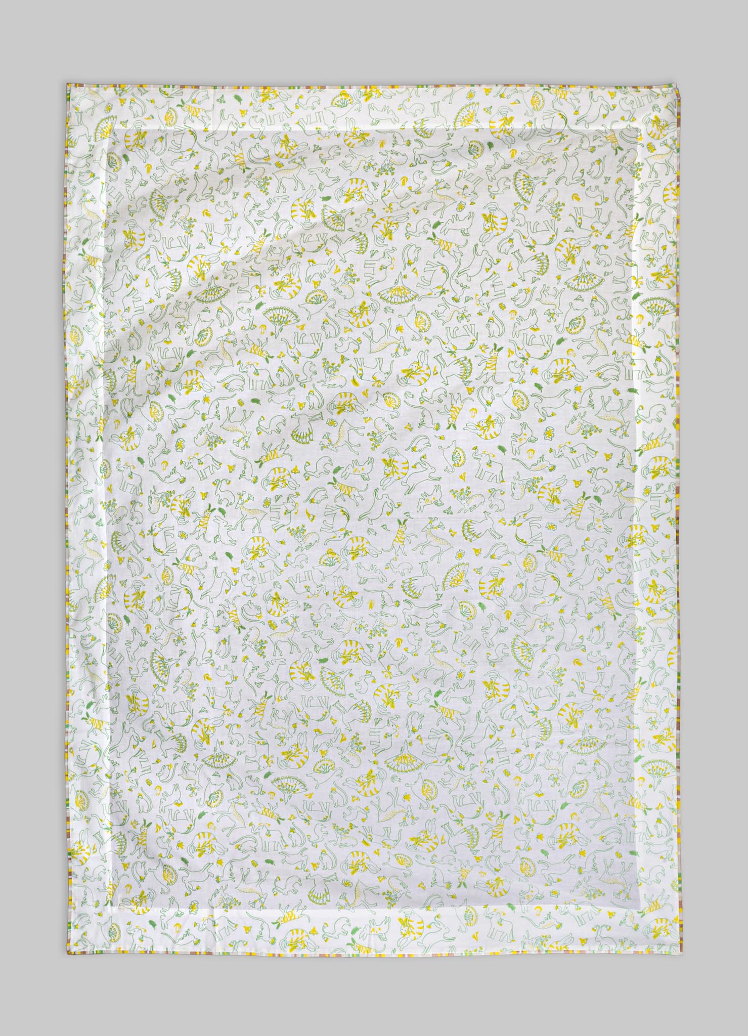 Cotton bed linen or blanket with a playful dinosaur pattern in yellow and green tones, featuring various dinosaurs and foliage motifs on a white background. The fabric has a smooth texture and is edged with a multicolored stitched border, in a casual and whimsical style.