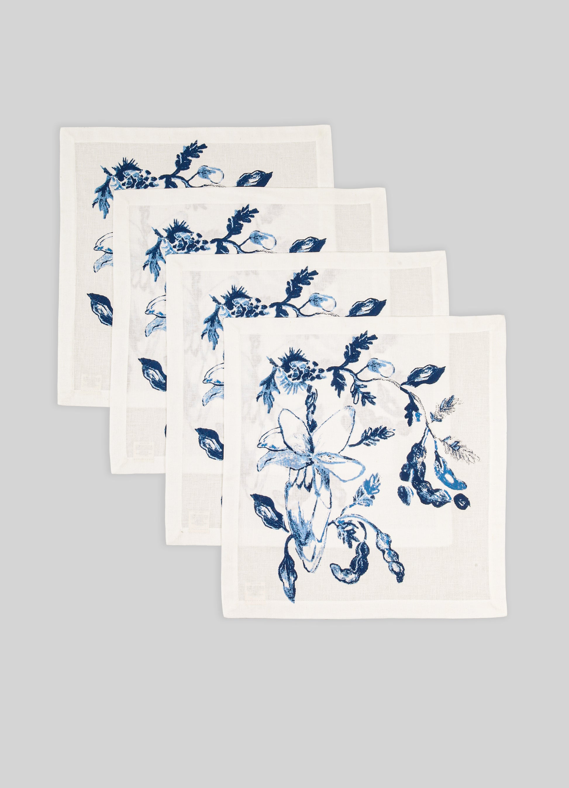 Set of four white napkins with blue floral patterns on a gray background