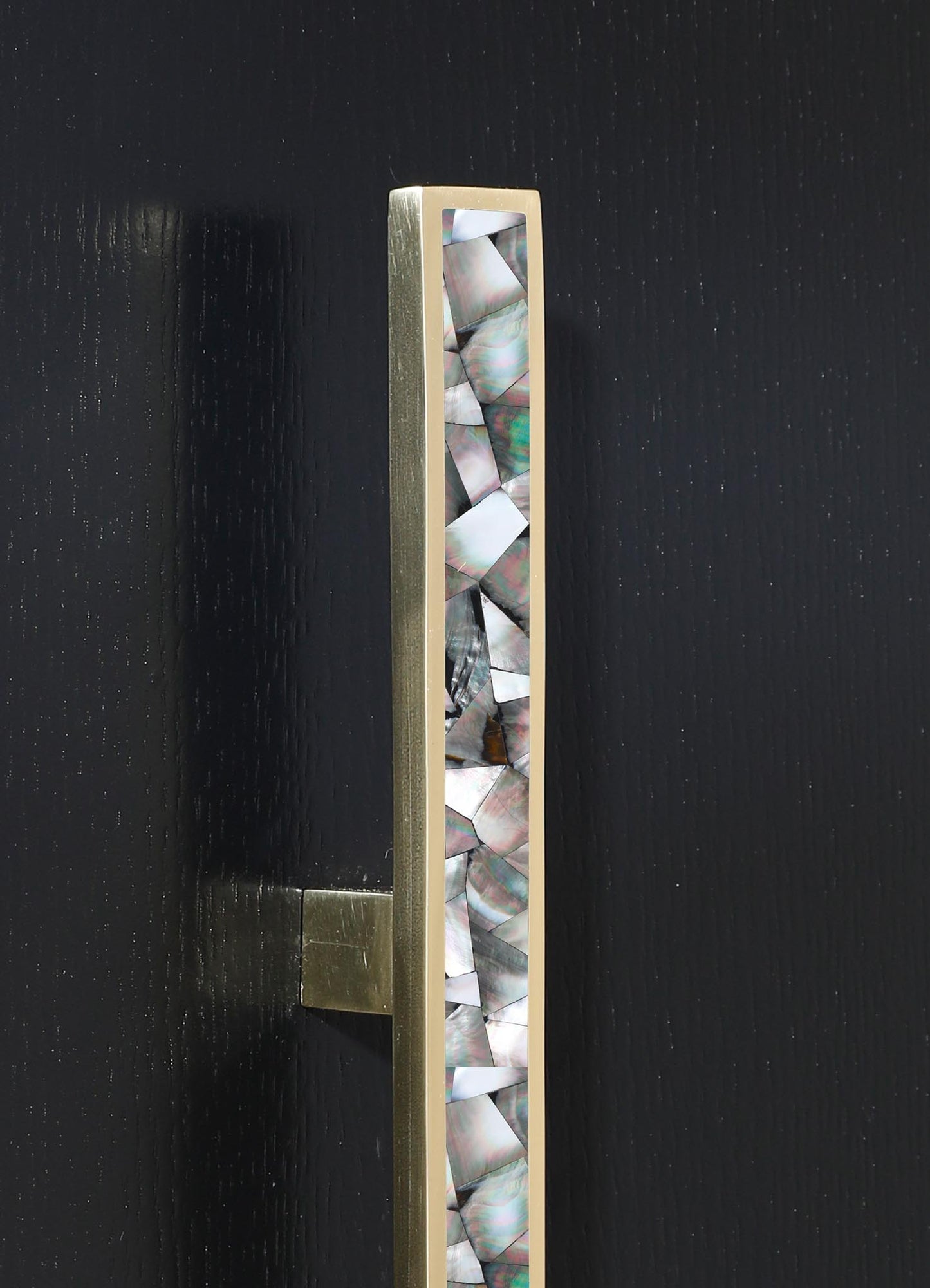 A tall, rectangular decorative object featuring a gold-toned frame with a slim profile and a panel of iridescent, geometric-shaped shell or mother-of-pearl inserts, set against a dark background.