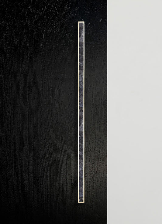 A vertical strip of dark marble with subtle veining is set on a textured black surface, bordered by a thin metallic edge. The design style is contemporary with a minimalist and sleek aesthetic.