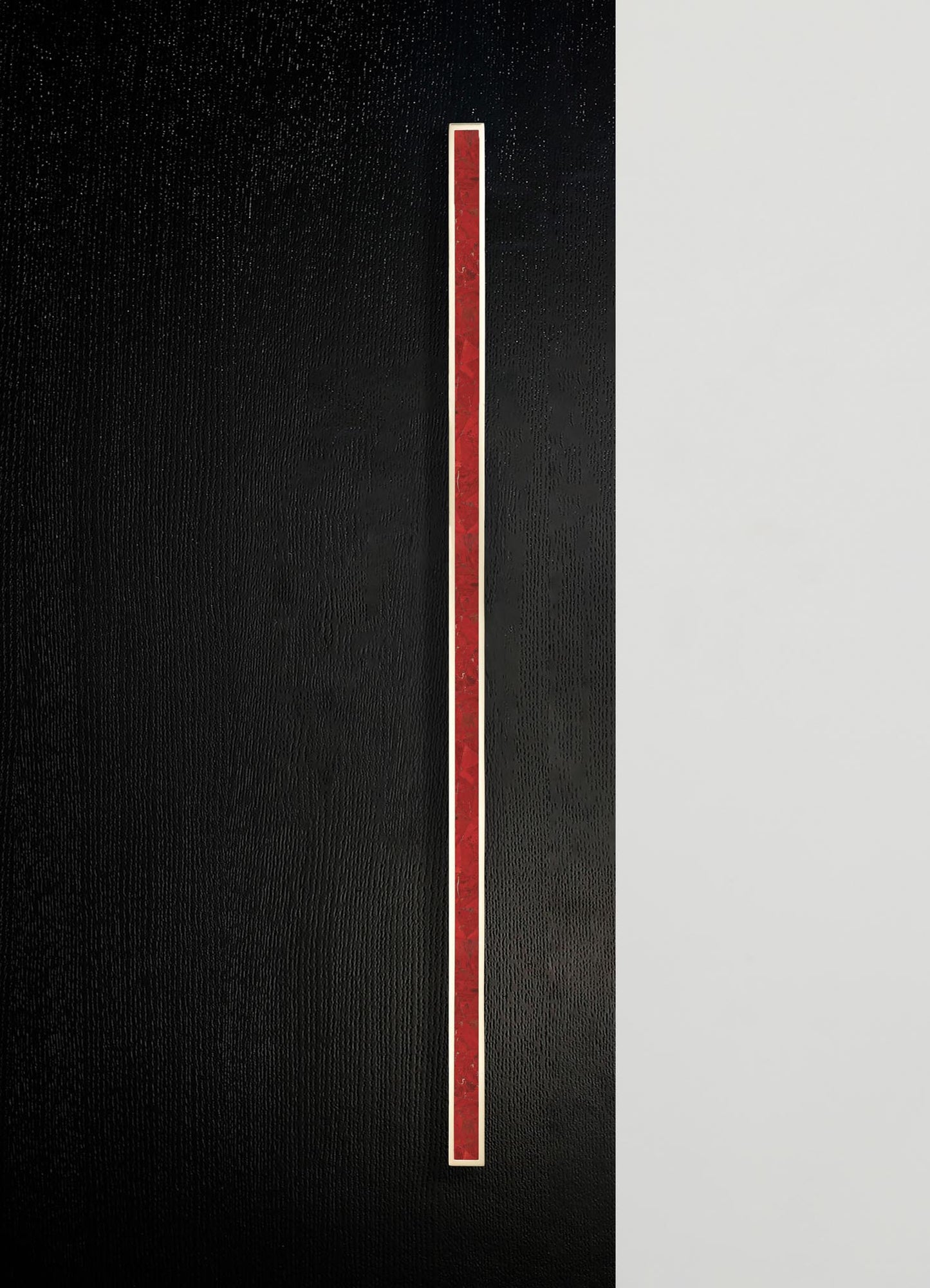 A vertical strip of red marble with a polished finish is set against a textured black background, creating a sleek, modern contrast with a matte white surface on the right. The design emphasizes minimalism and contemporary style with bold color accents and clean lines.