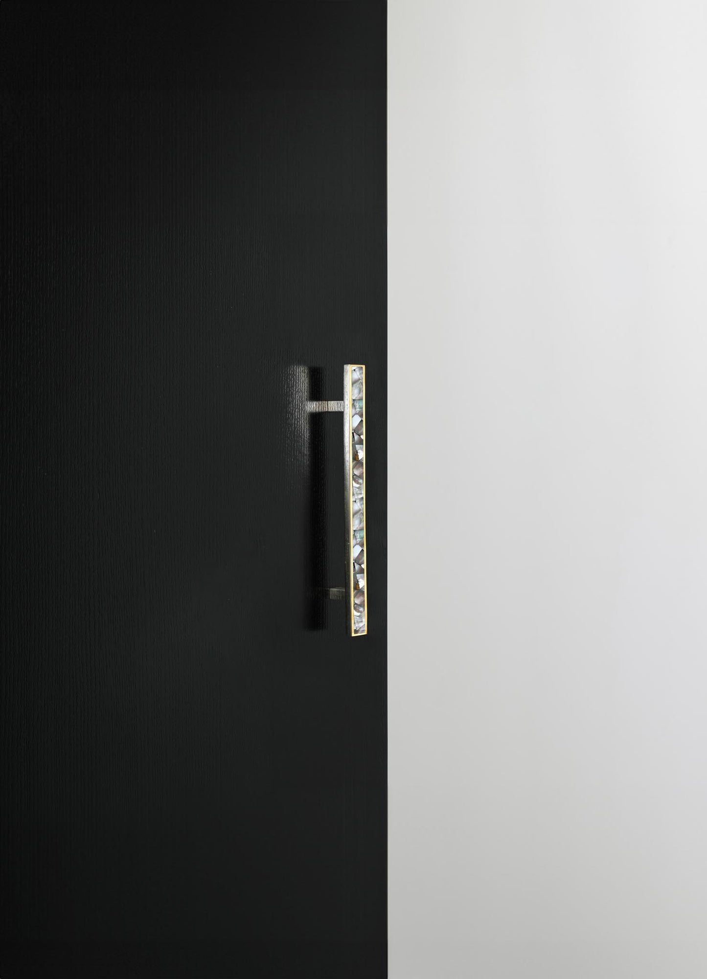 A modern kitchen cabinet with a black textured finish on one side and a smooth white surface on the other, featuring a vertical handle with a gold frame and decorative glass or gemstone inlay.