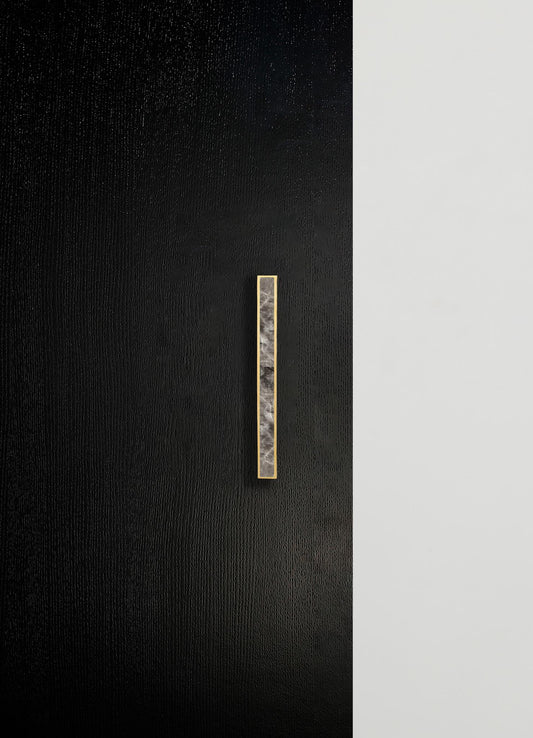 A minimalist wall design featuring a black textured surface on the left and a smooth white surface on the right, with a vertical marble and brass wall handle or accent strip positioned on the black side.