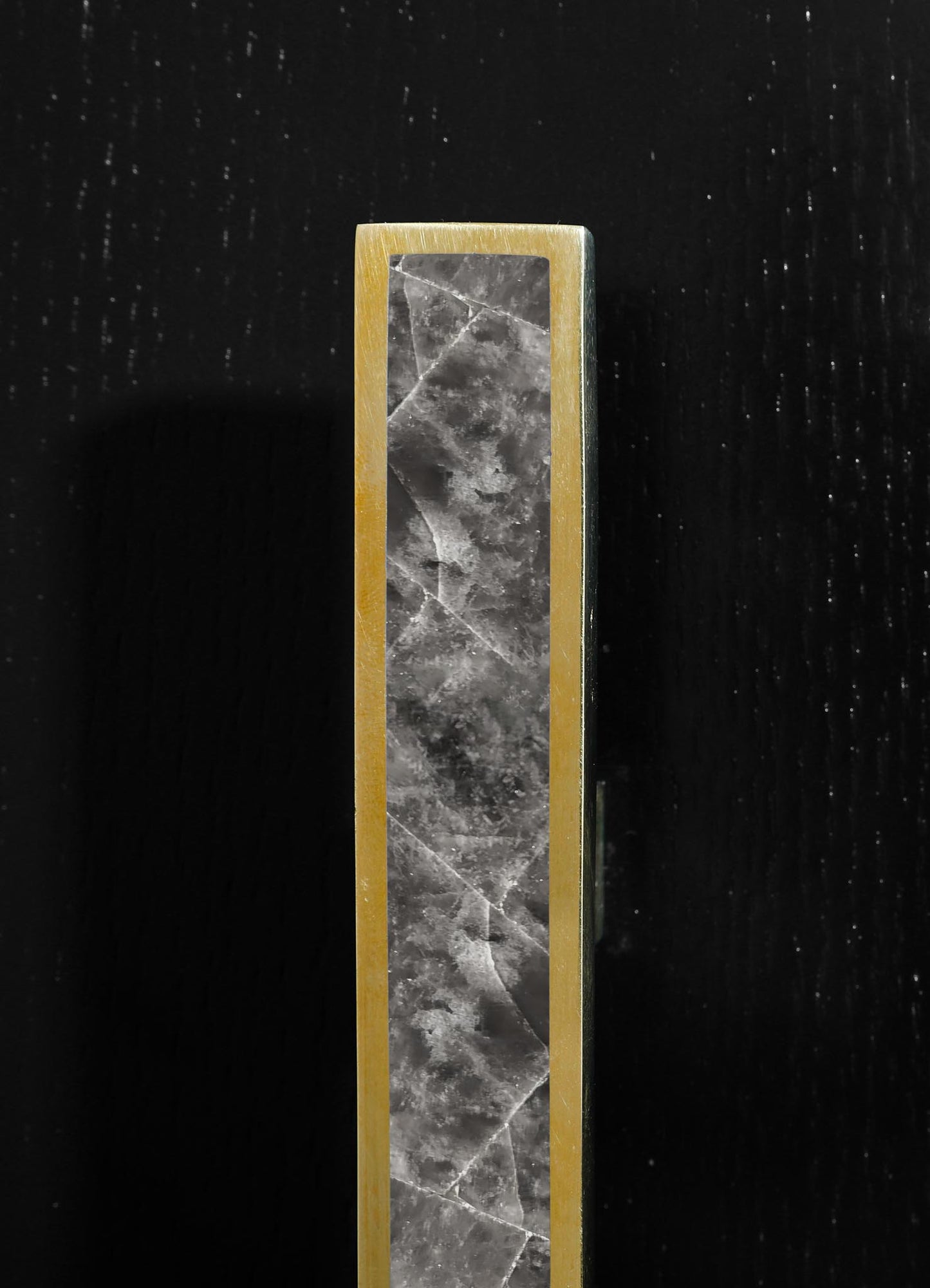 A tall, slender candle holder made of brass with a rectangular black marble insert featuring natural gray and white veining. The minimalist design emphasizes a contemporary style with metallic and stone materials.