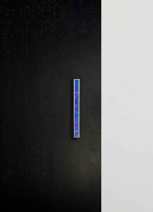 A modern door with a textured black surface and a vertical blue inlay handle with gold edges. The opposite side features a smooth white surface.