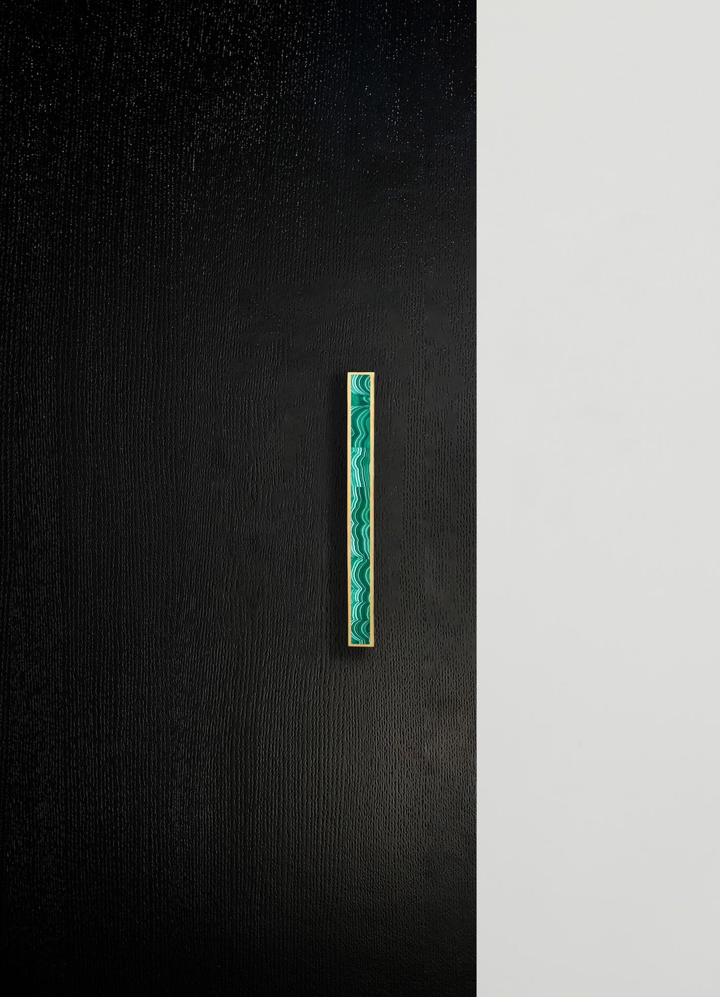 A modern wall with a textured black panel and a contrasting smooth white section, featuring a narrow vertical decorative strip with a green and turquoise marbled pattern framed in gold.