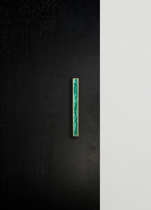 A modern wall with a textured black panel and a contrasting smooth white section, featuring a narrow vertical decorative strip with a green and turquoise marbled pattern framed in gold.