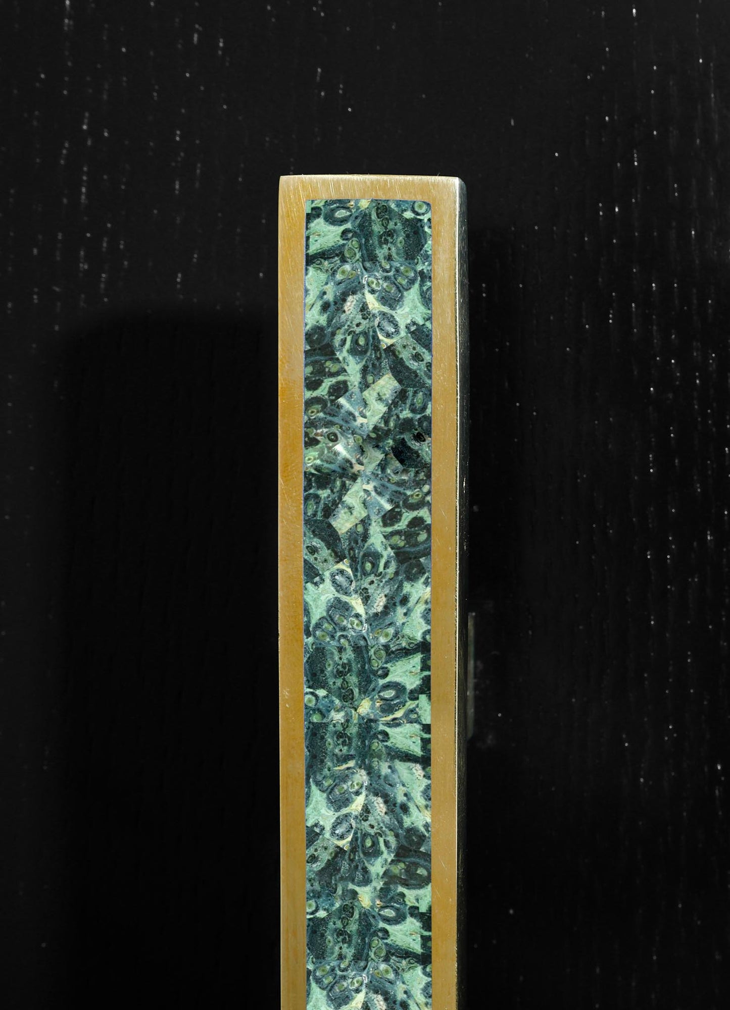 A rectangular perfume bottle with a gold-colored metal frame and a marble-patterned glass panel featuring shades of green and black, on a black background.