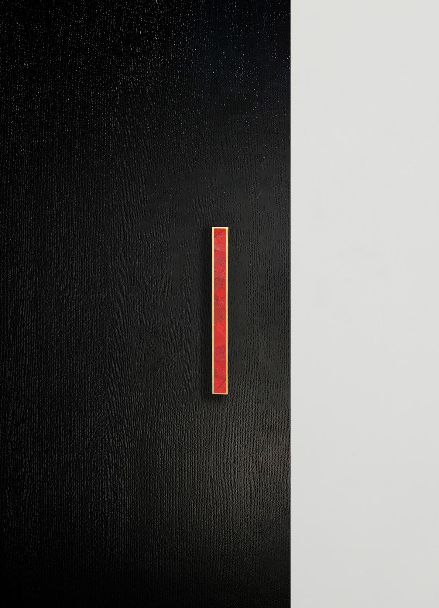 A black textured wall with a slim, vertical red marble and gold metal accent strip mounted in the center. The design has a contemporary and minimalist style with contrasting color tones and clean lines.