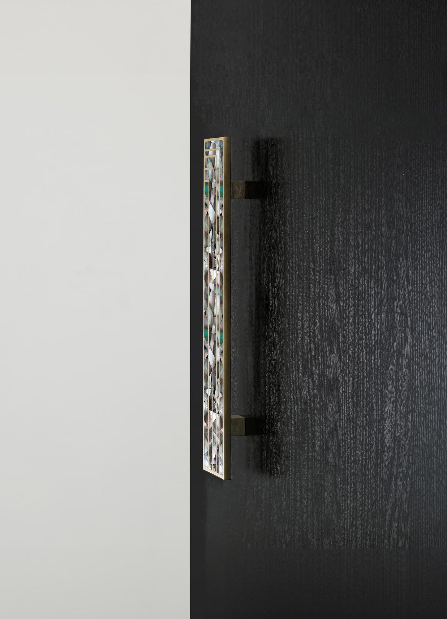 A decorative wall sconce featuring a geometric design with iridescent glass or acrylic elements and a brass or gold-toned frame mounted on a textured black wall. The fixture has a modern style with a focus on metallic and reflective surfaces.
