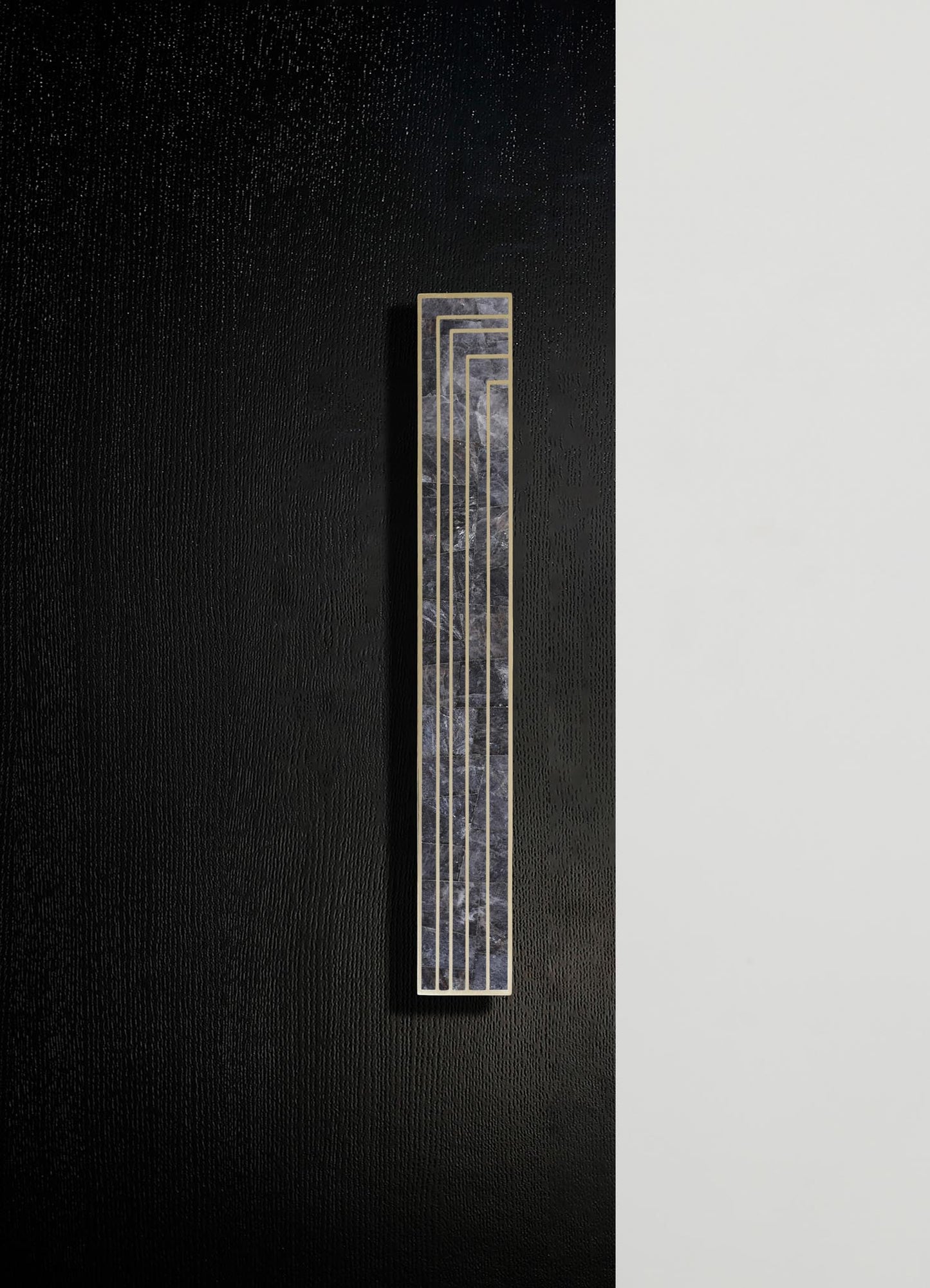 A rectangular wall plaque with a dark, marbled surface featuring metallic gold linear accents arranged in a geometric pattern, mounted on a black textured wall with a contrasting white vertical section.