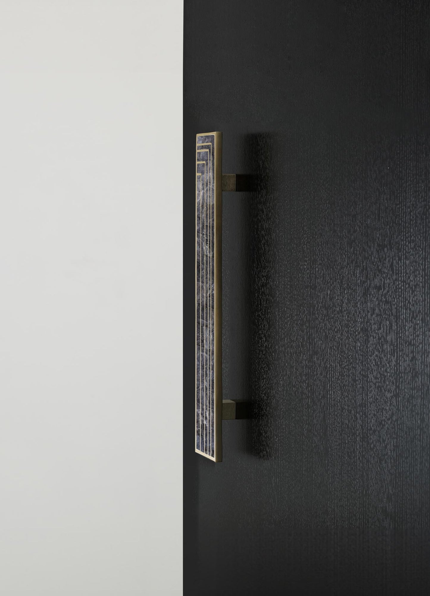 A decorative wall sconce with a rectangular brass frame and geometric cutout pattern, featuring a dark, opaque glass or stone inlay, mounted on a black textured wall.