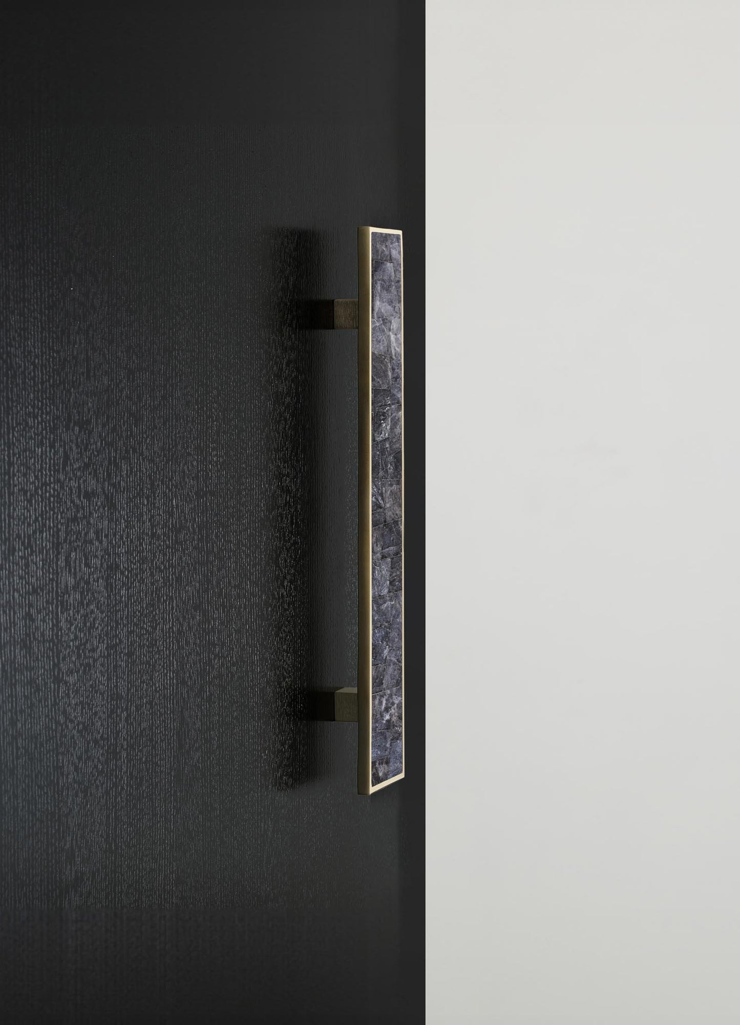 A modern wall-mounted picture light with a rectangular brass frame and a dark stone accent in the center, installed on a textured black wall with a white background.