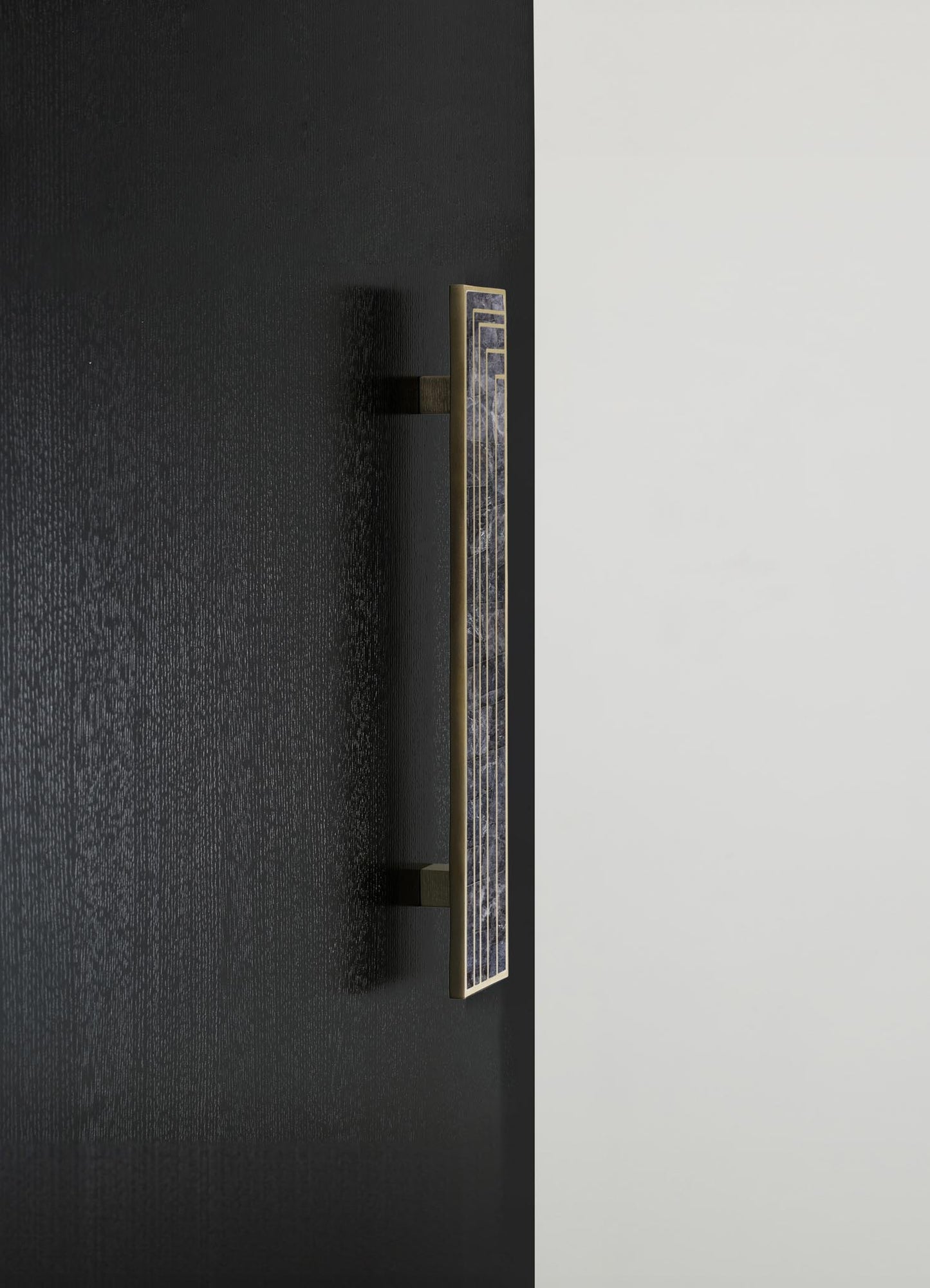 A decorative wall sconce featuring a vertically elongated rectangular design with a brass frame and a patterned panel in shades of blue and gray marble. The fixture is mounted on a black wall, creating a contemporary aesthetic.