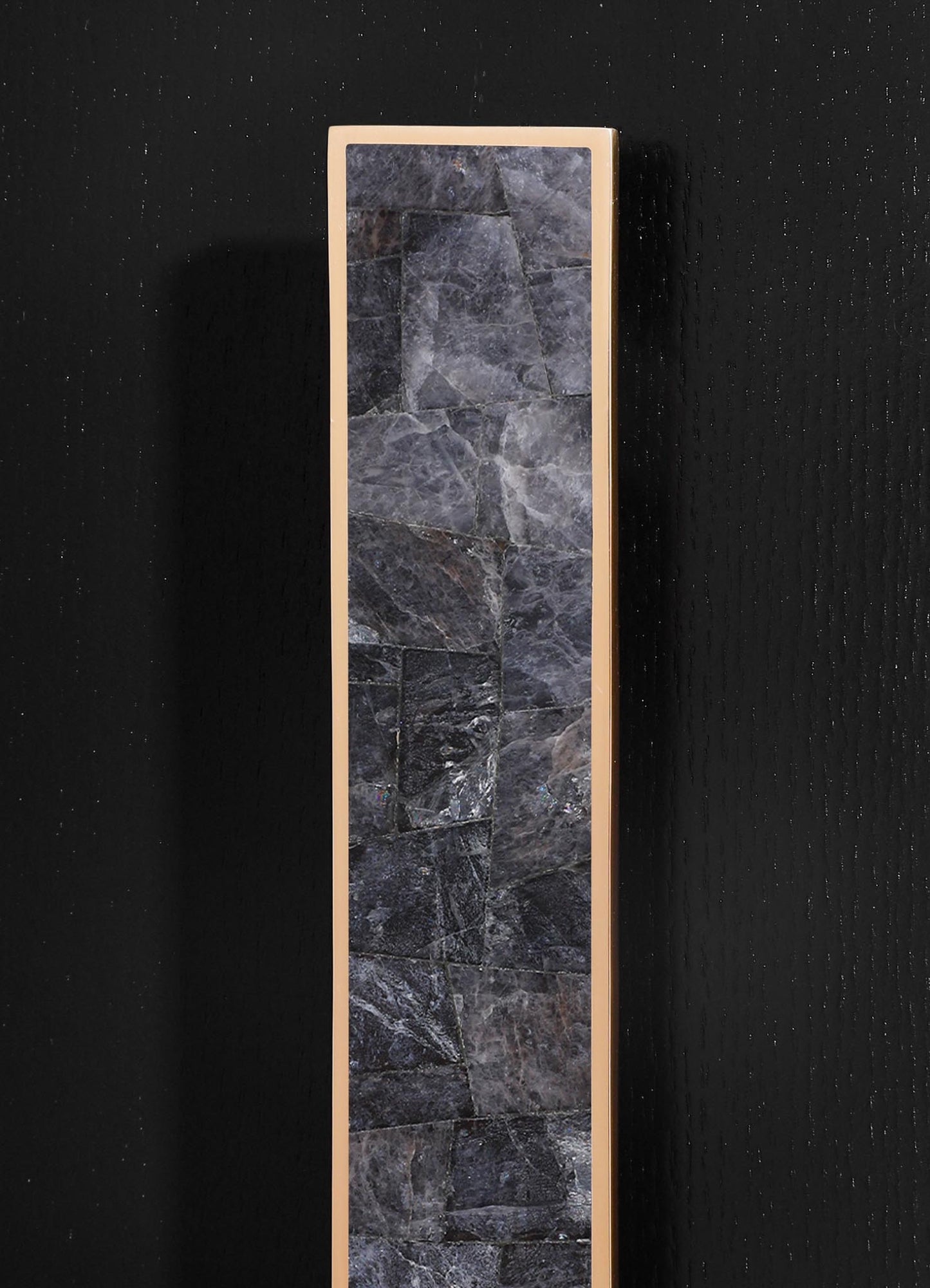 A tall rectangular mirror with a beige or light-colored frame featuring a stone or marble pattern on the surface. The mirror is mounted on a black wall with a textured finish.