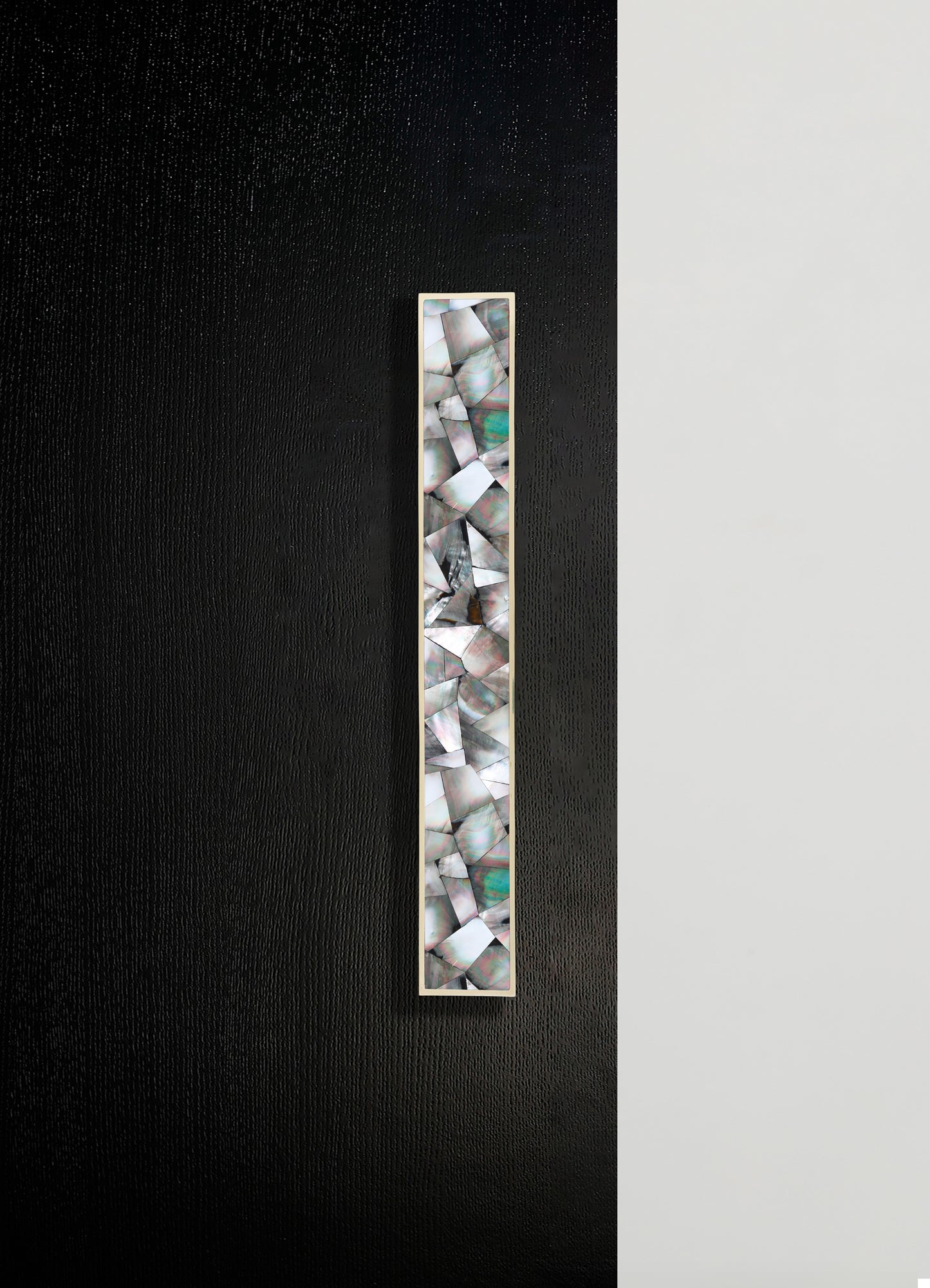 A tall decorative panel featuring inlaid shells with iridescent, multicolored patterns set within a slim, rectangular frame, displayed against a two-tone black and white wall.