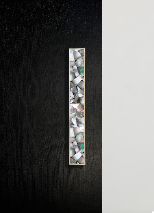 A tall decorative panel featuring inlaid shells with iridescent, multicolored patterns set within a slim, rectangular frame, displayed against a two-tone black and white wall.