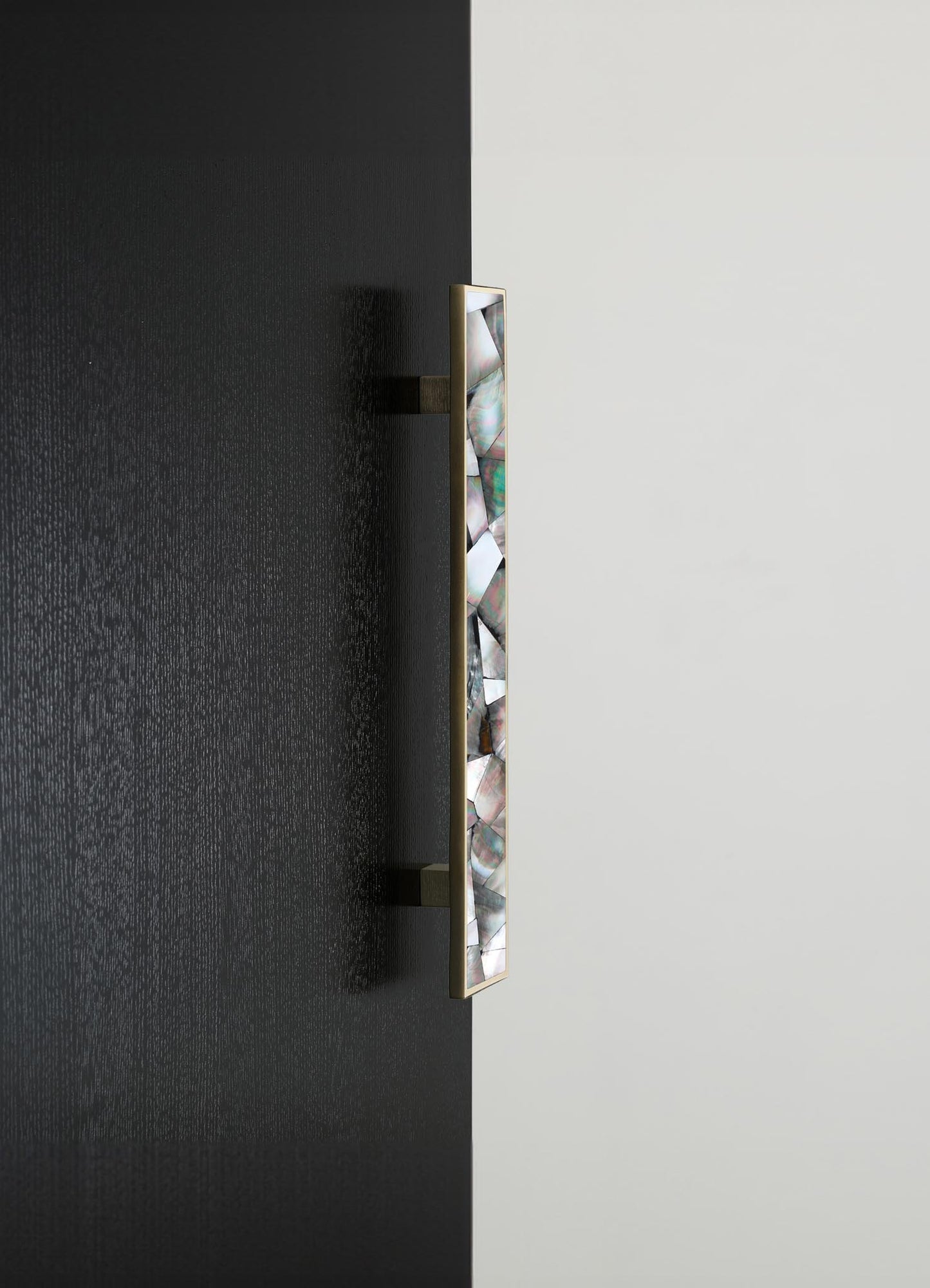 A vertical wall-mounted sculpture with an abstract design, featuring a slim, rectangular shape framed in gold. The artwork displays a pattern of iridescent, mosaic-like shells or stones with a pearlescent finish, set against a black and white background.