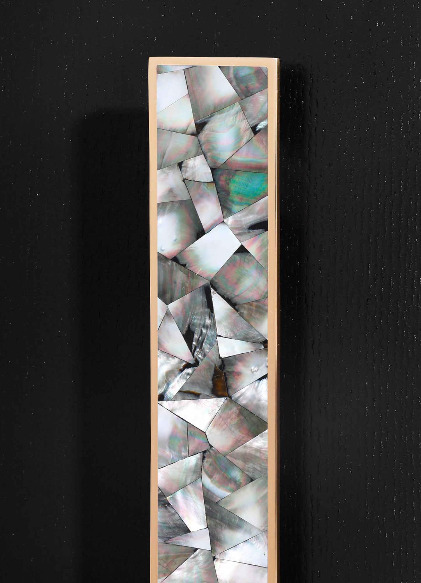 A decorative panel featuring an iridescent abalone shell inlay with geometric, shard-like patterns and thin metallic framing, set against a black textured background.