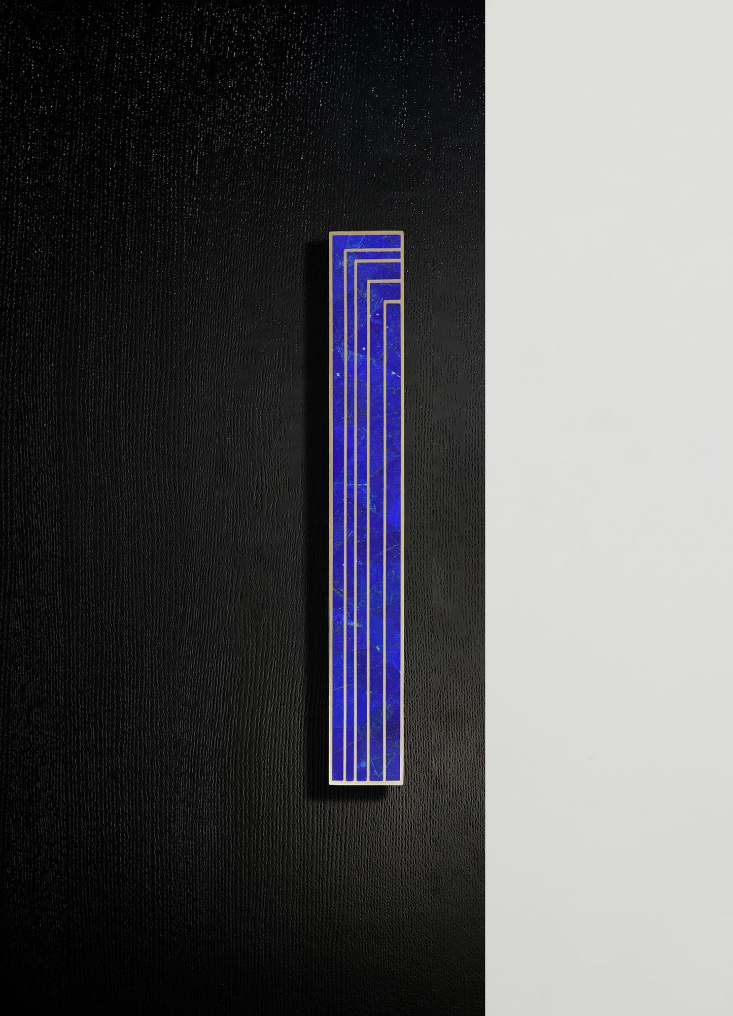 A tall, rectangular wall art piece features a deep blue, marble-like surface with gold geometric lines, set against a black textured wall with a contrasting white panel.