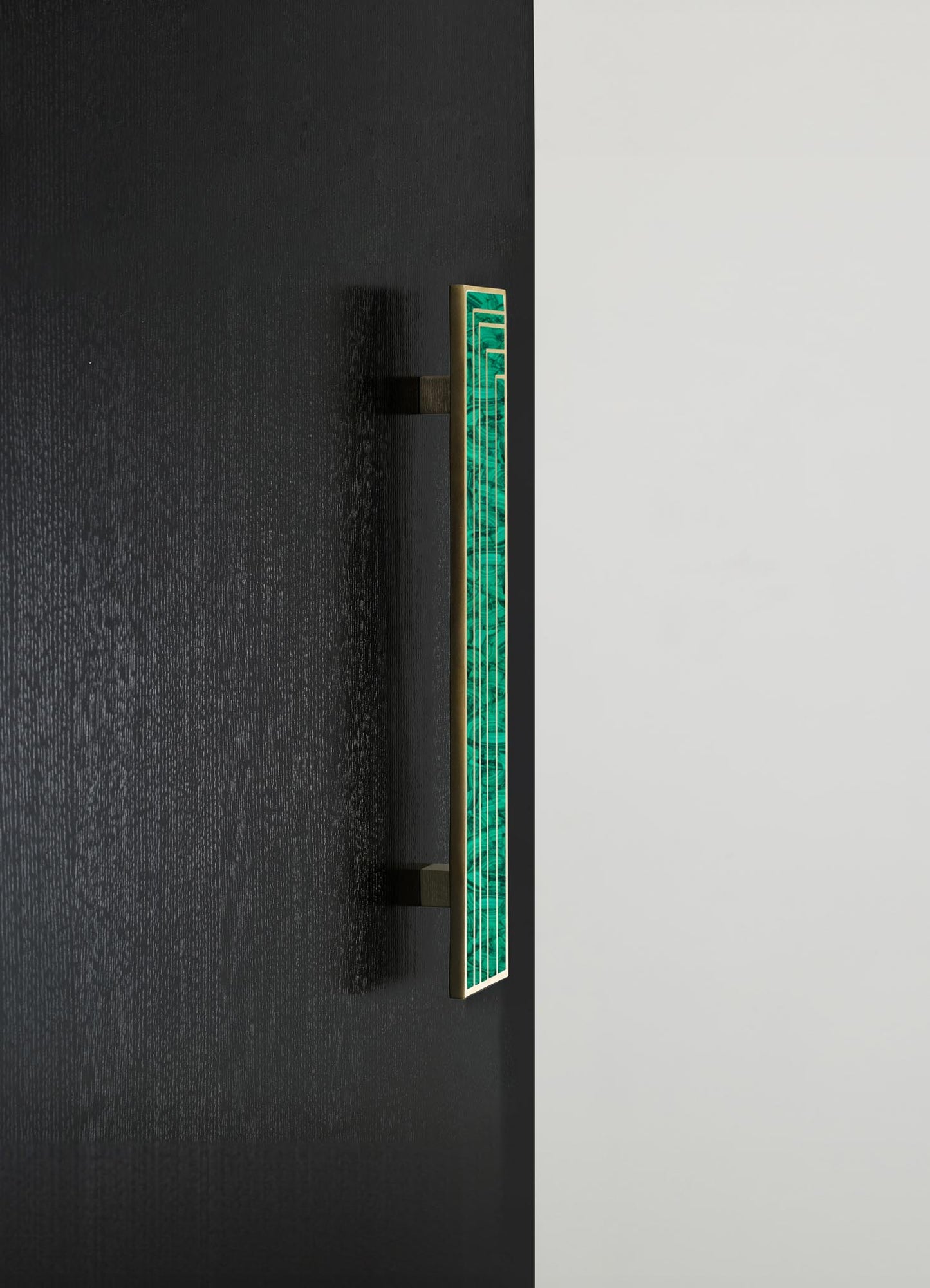 A decorative wall-mounted panel with a geometric pattern in green malachite-like material and a gold frame, attached to a black wall with contrasting white background.