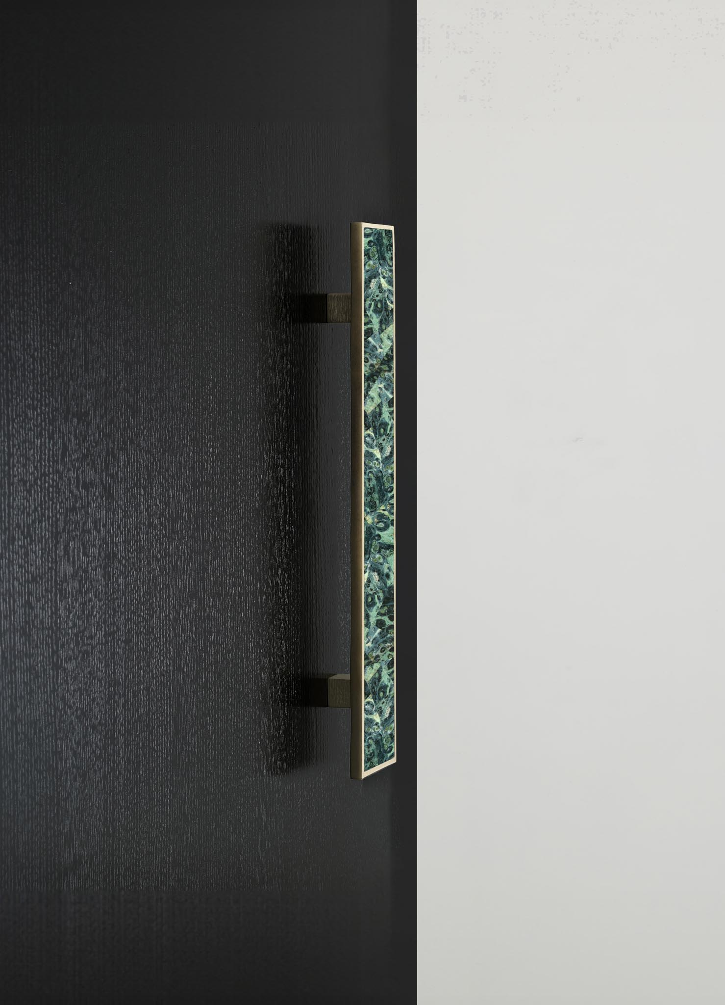 A decorative wall sconce featuring a rectangular brass frame with a patterned inlay in green and blue hues, mounted on a contrasting black and white wall.