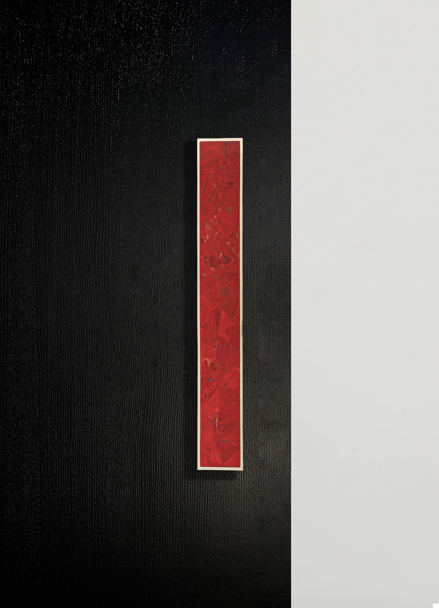 A rectangular wall art piece featuring a red, textured pattern set within a white frame, mounted on a wall with a black textured section adjacent to a smooth white surface.