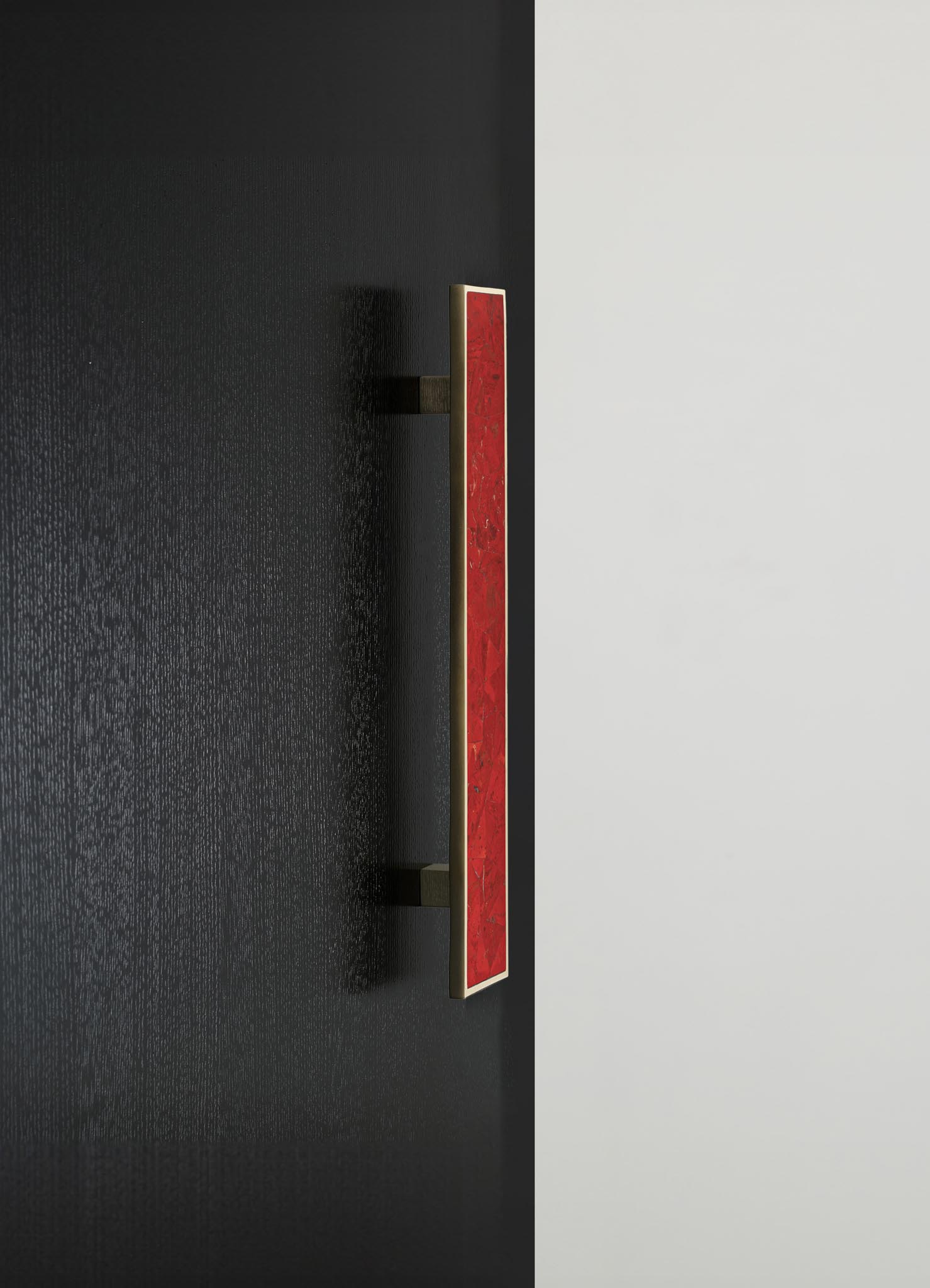 A wall-mounted light fixture with a rectangular red glass shade and a metal frame in a contemporary style, installed on a black textured wall next to a smooth white surface.
