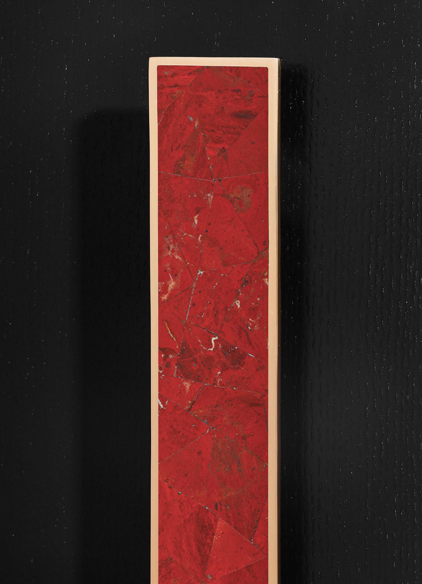 A vertical rectangular panel featuring a red marble surface with natural veining and geometric patterns, framed in a light-colored border, set against a black textured background.
