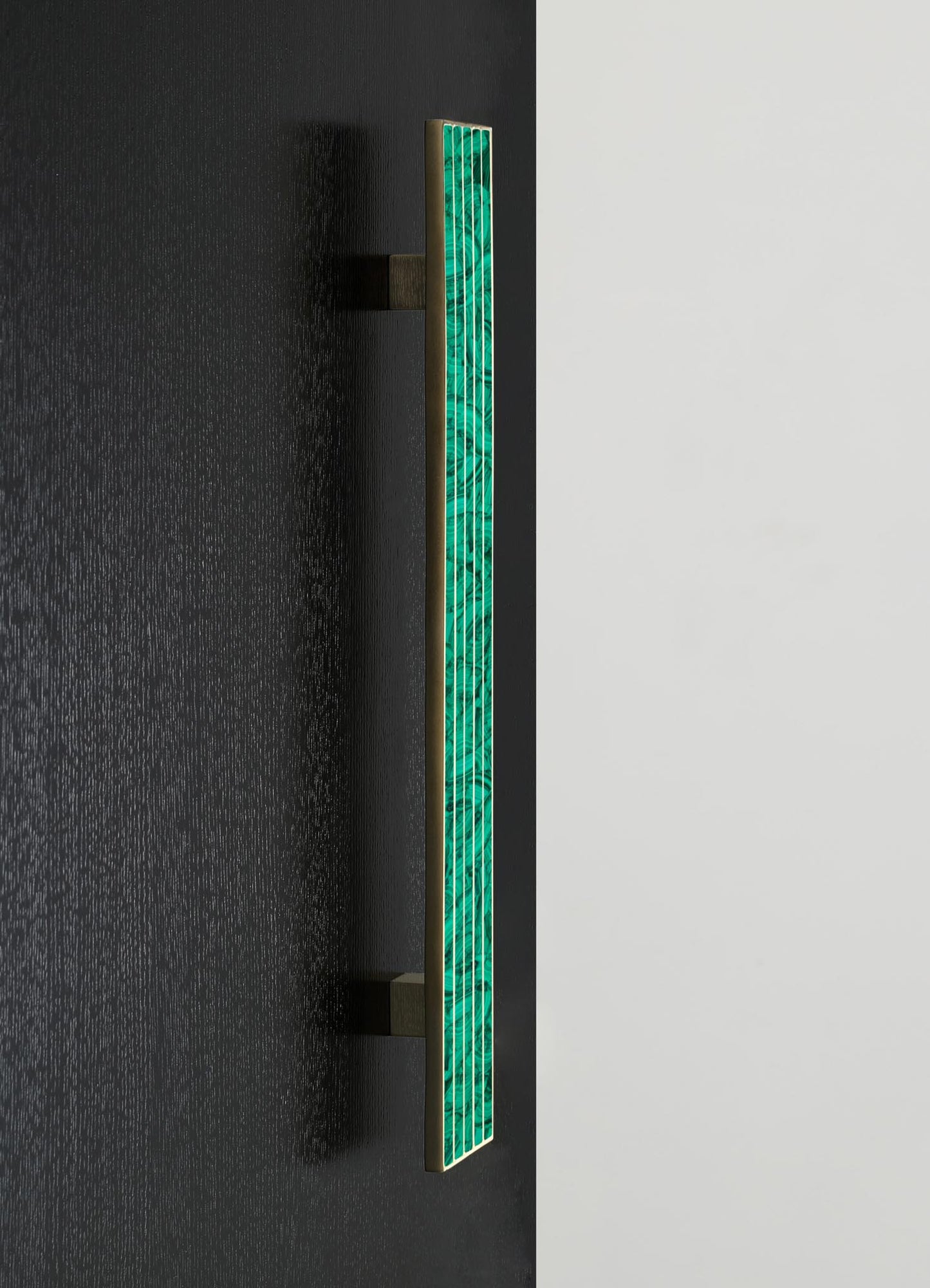 A modern wall sconce with a brass finish and a vertical strip of teal-hued onyx or glass in a geometric pattern, mounted on a wall with contrasting dark and light panels.