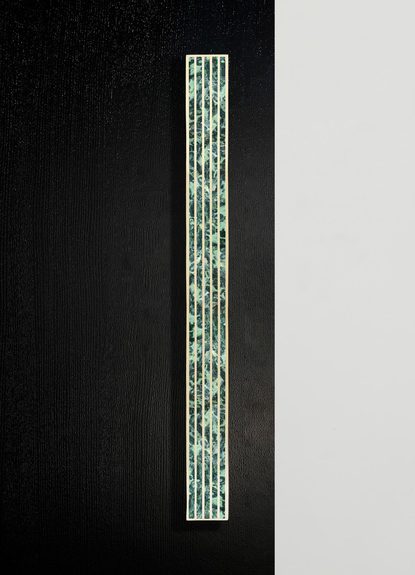 Vertical decorative wall panel with a geometric pattern and a combination of brass and green marble-like materials, mounted on a black textured background.