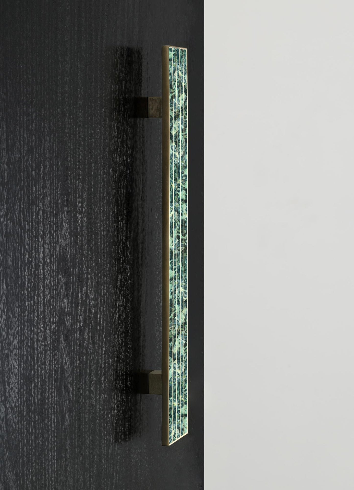 A vertical wall-mounted sconce with a rectangular shape, featuring a decorative mosaic pattern with green and blue tones and framed in brass, mounted on a black wall.
