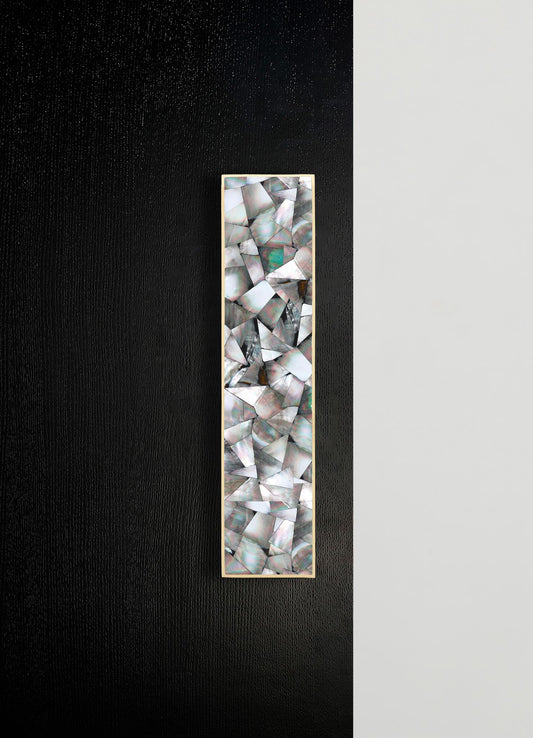 A rectangular wall mirror with a frame made of iridescent abalone shell fragments arranged in a mosaic pattern, mounted on a textured black wall. The mirror's design features organic, shimmering motifs that evoke a contemporary aesthetic.