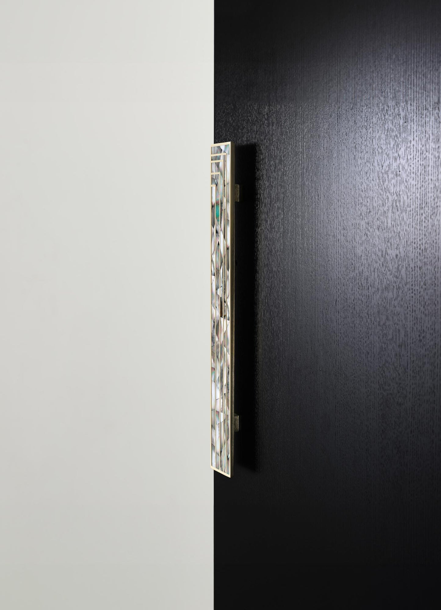 A decorative wall sconce with a rectangular, geometric design featuring iridescent or glass panels, mounted on a wall with contrasting black and white surfaces.