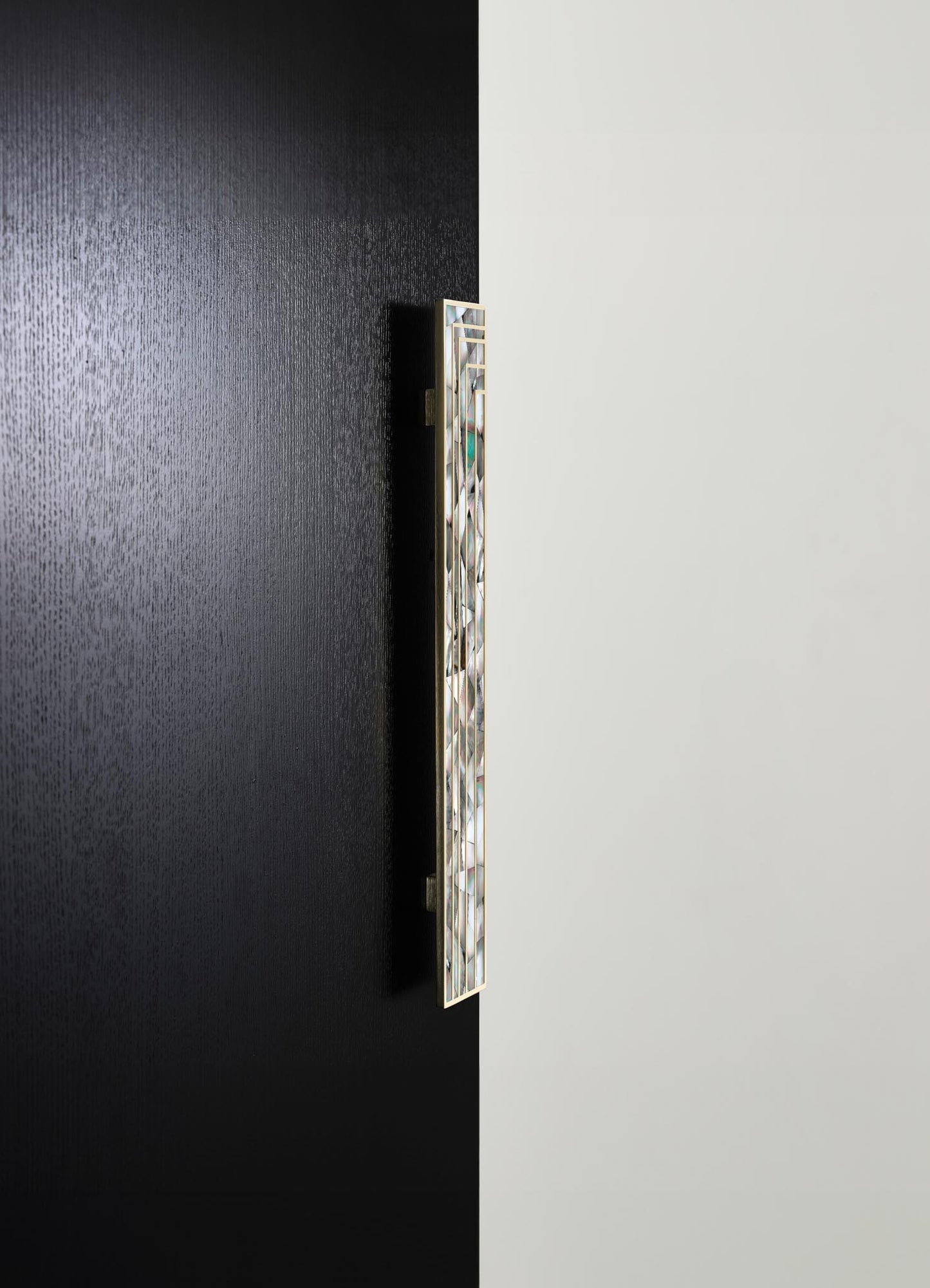 A wall-mounted decorative sconce with a rectangular shape, featuring a frame of metallic gold and inlaid with mother-of-pearl or similar iridescent material, set against a black and white wall.