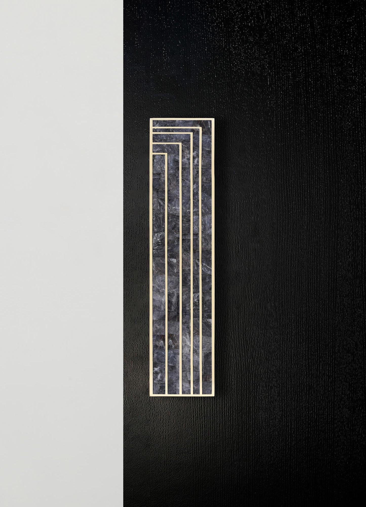 A decorative wall panel featuring a rectangular shape combining black marble with gray veining and a metal frame in a geometric, stepped pattern. The panel is mounted on a contrasting black textured wall with a minimalist aesthetic.