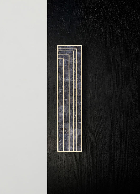 A decorative wall panel featuring a rectangular shape combining black marble with gray veining and a metal frame in a geometric, stepped pattern. The panel is mounted on a contrasting black textured wall with a minimalist aesthetic.