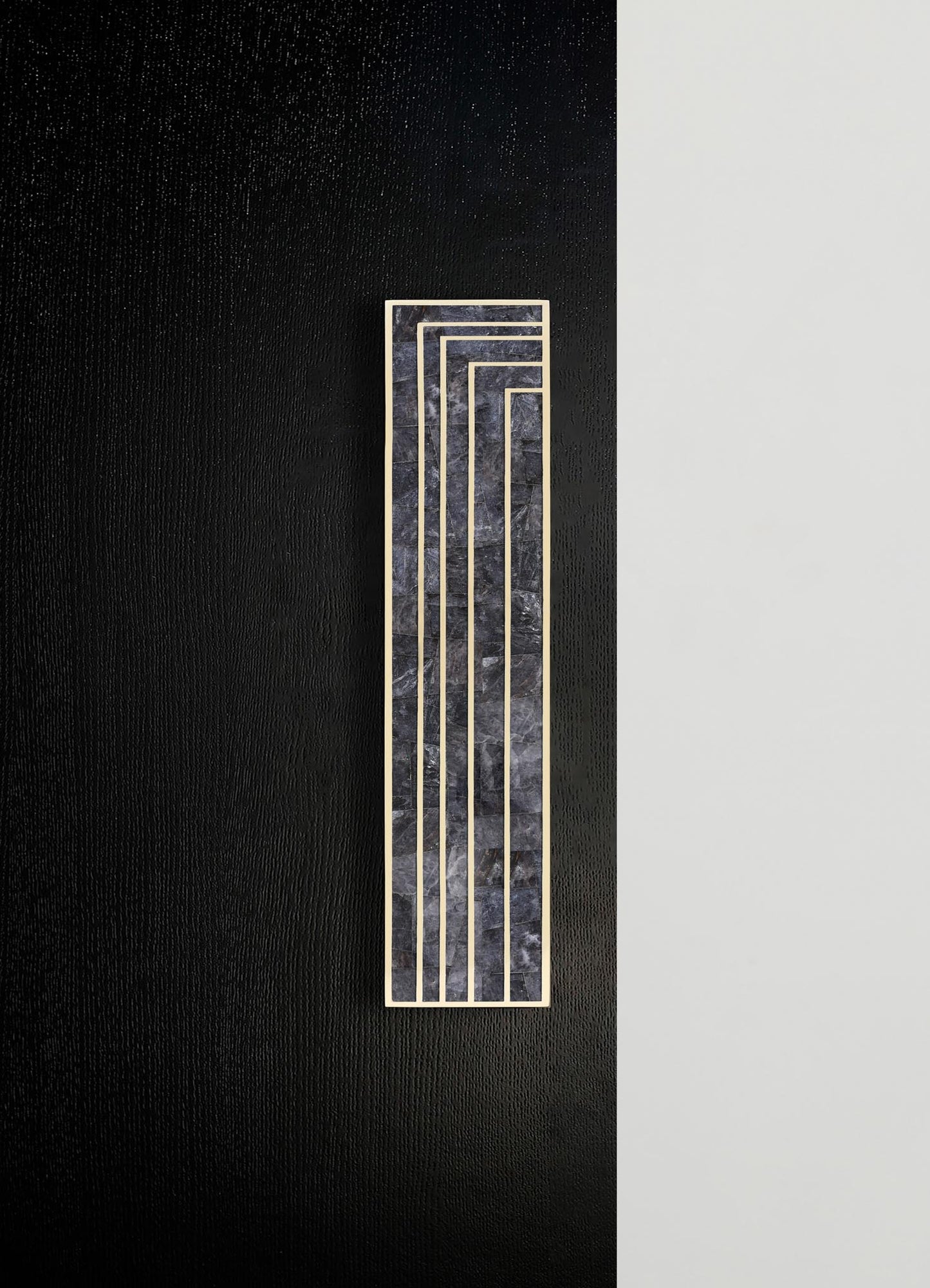 A decorative wall panel featuring black marble with white veining accented by a geometric pattern of thin, contrasting metallic gold lines. The panel is mounted on a wall with a textured black section adjacent to a smooth, light-colored surface, creating a contemporary and minimalist design.
