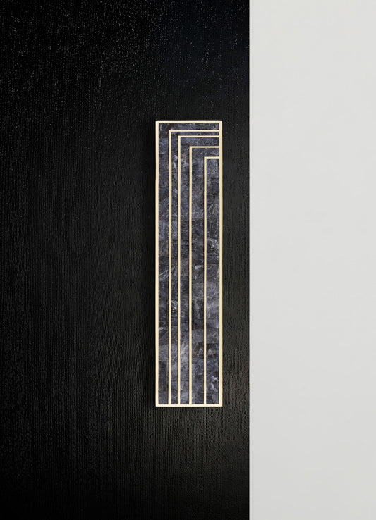 A decorative wall panel featuring black marble with white veining accented by a geometric pattern of thin, contrasting metallic gold lines. The panel is mounted on a wall with a textured black section adjacent to a smooth, light-colored surface, creating a contemporary and minimalist design.