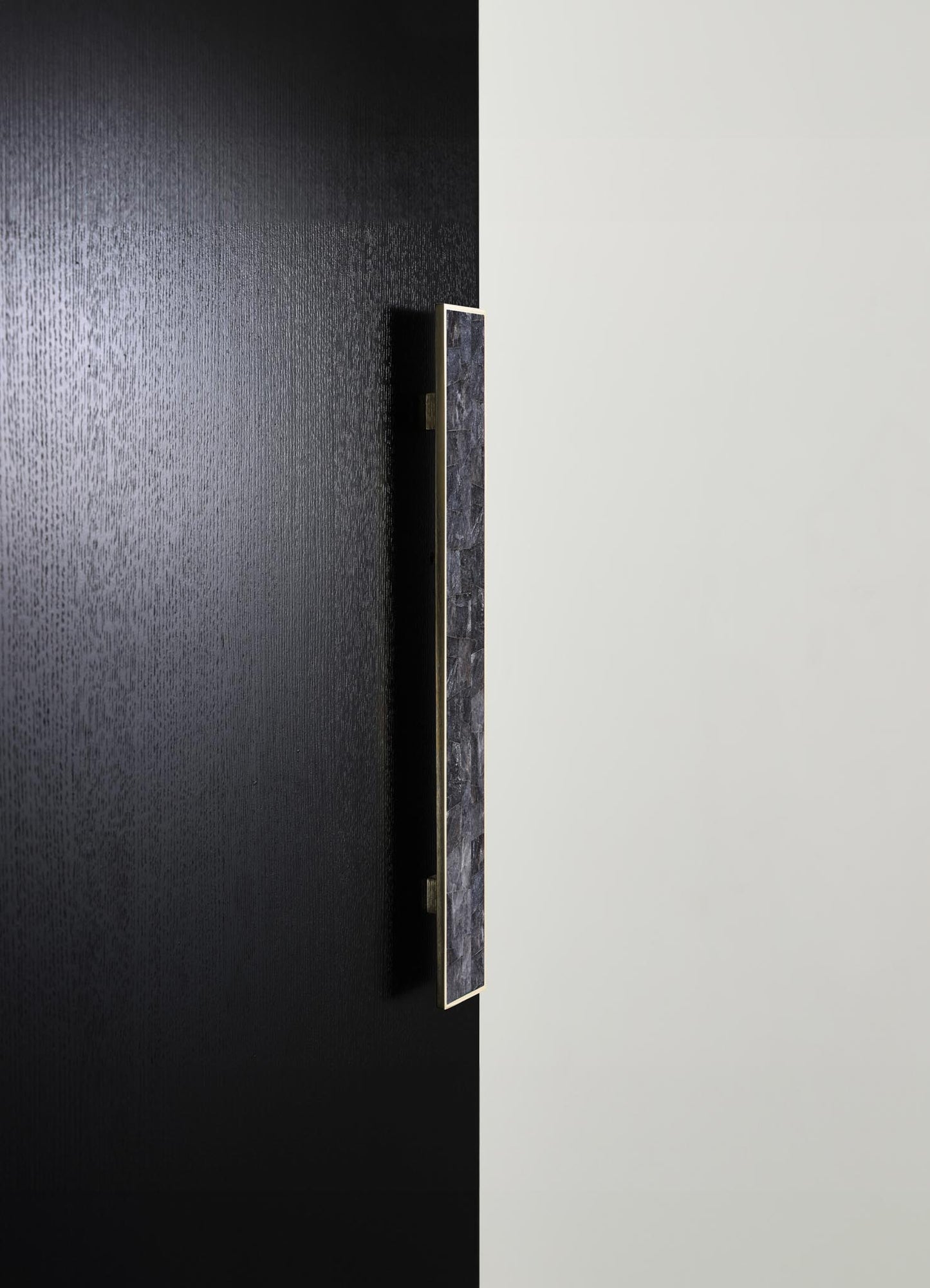 A modern door handle mounted on a black textured door, featuring a slim rectangular design with a metallic finish and stone inset in shades of gray and black.