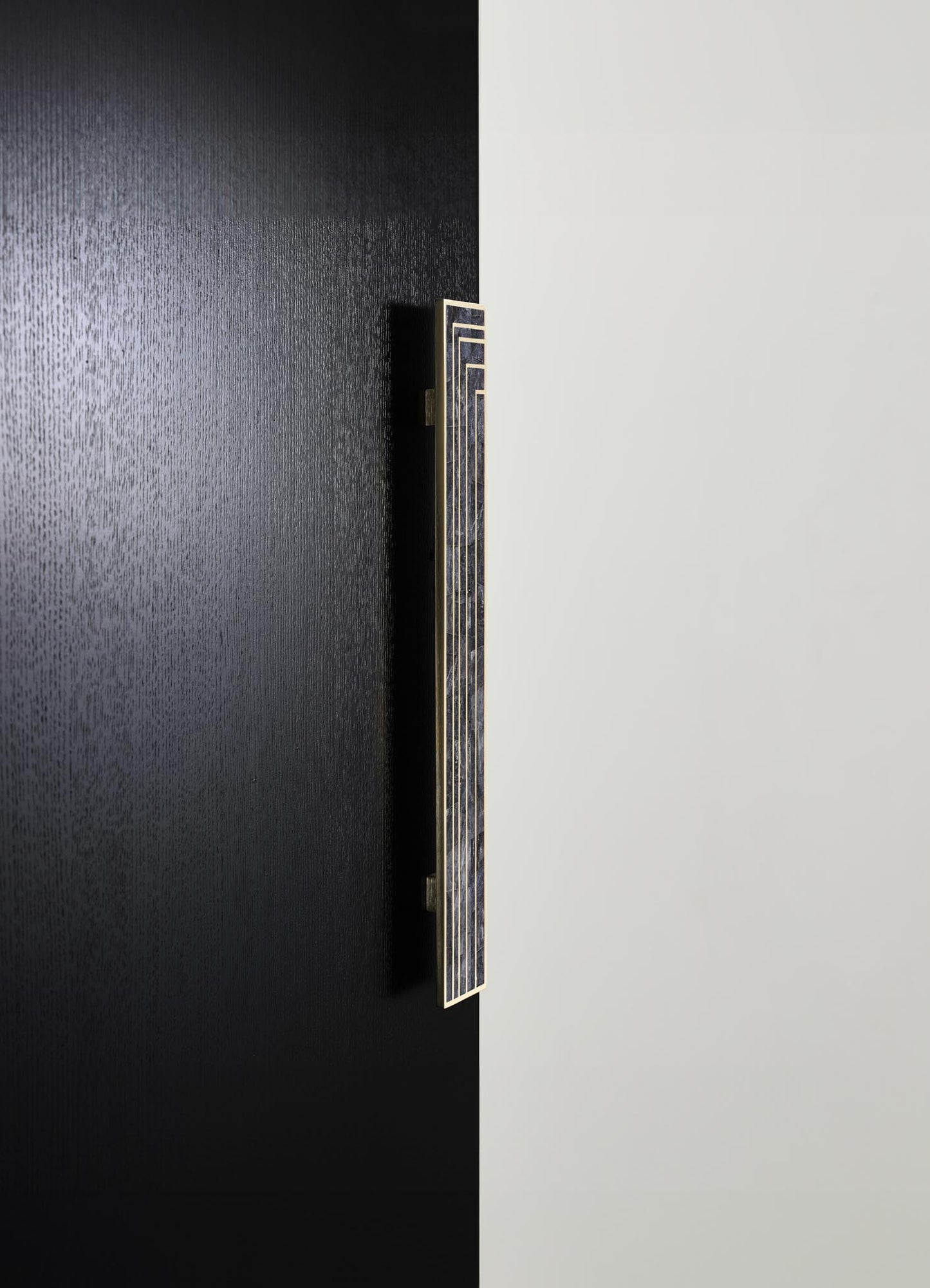 A modern door handle with a sleek, rectangular design featuring black and gold accents, mounted on a contrasting black and white panel door. The handle has a contemporary style with geometric lines.