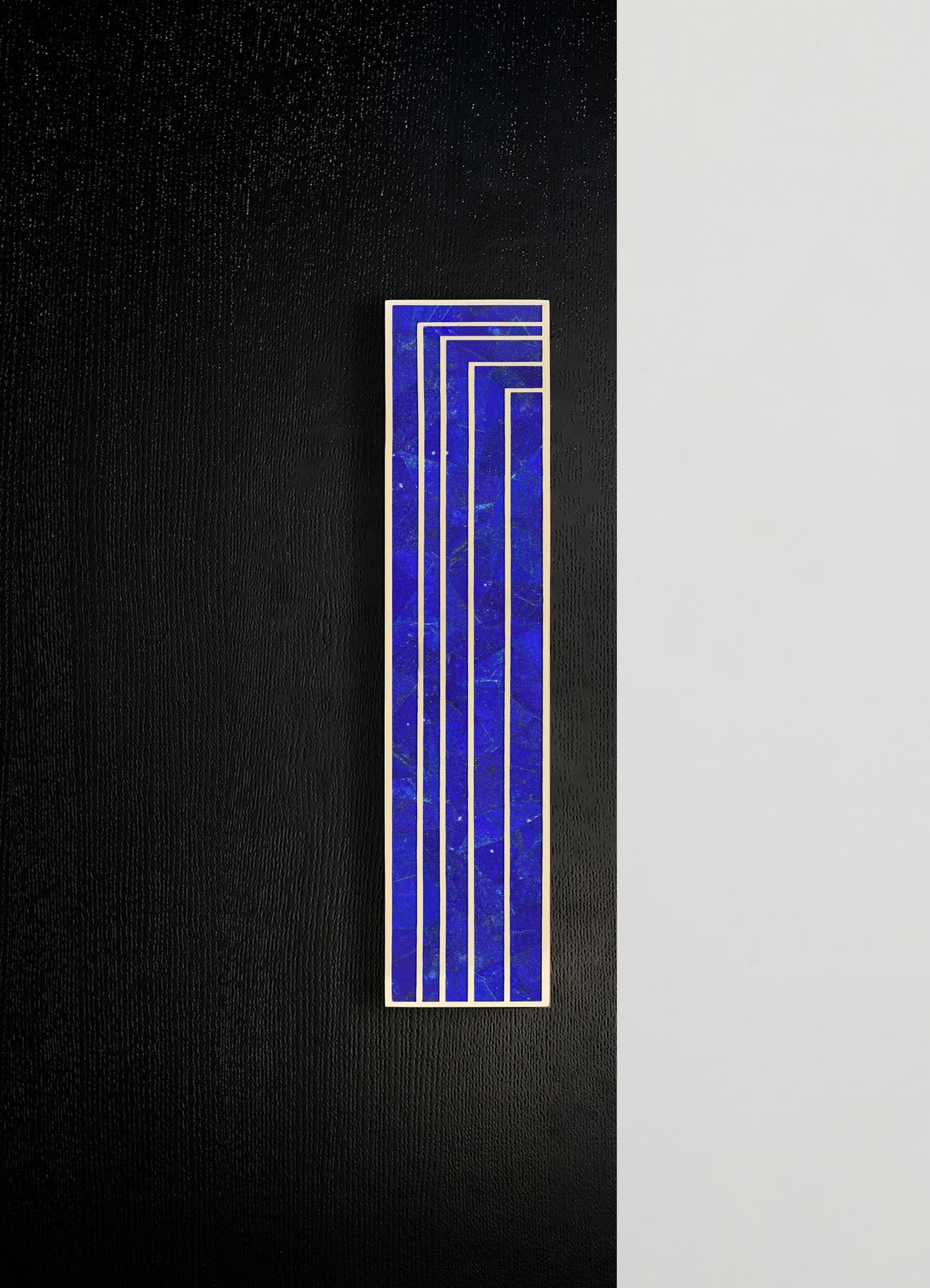 A rectangular ceramic tile with a vibrant royal blue marbled pattern and white geometric lines, set against a background of black and light gray textured surfaces.