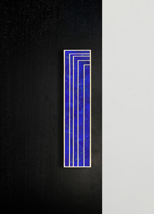 A rectangular ceramic tile with a vibrant royal blue marbled pattern and white geometric lines, set against a background of black and light gray textured surfaces.