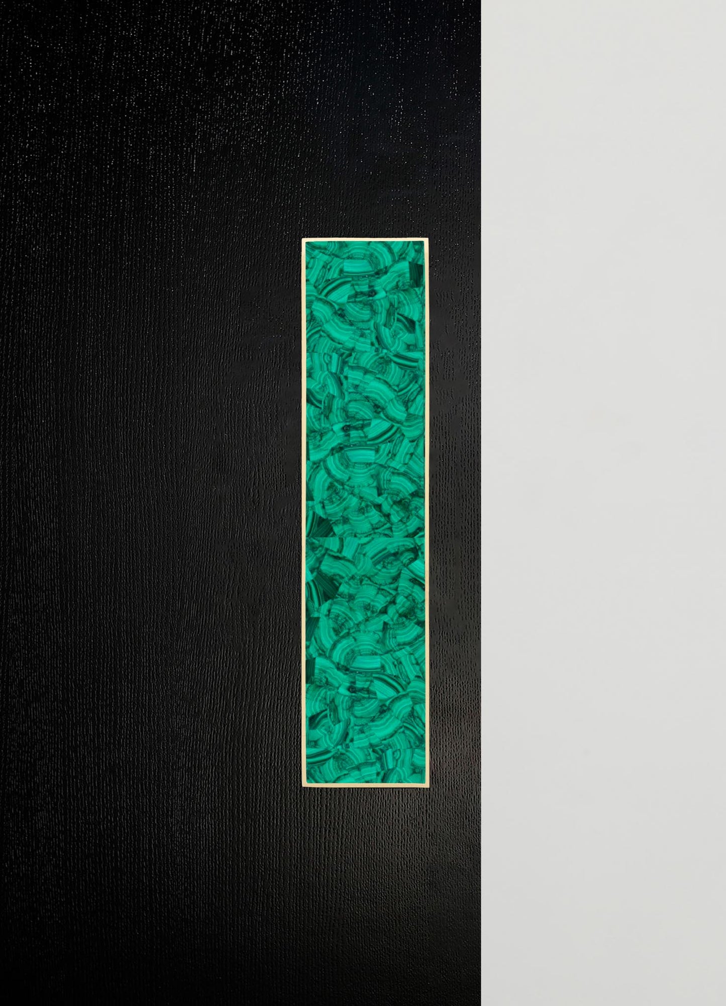 A tall, rectangular decorative art piece with a green malachite-inspired pattern framed in light wood, mounted on a wall with a bold black and neutral gray color contrast.