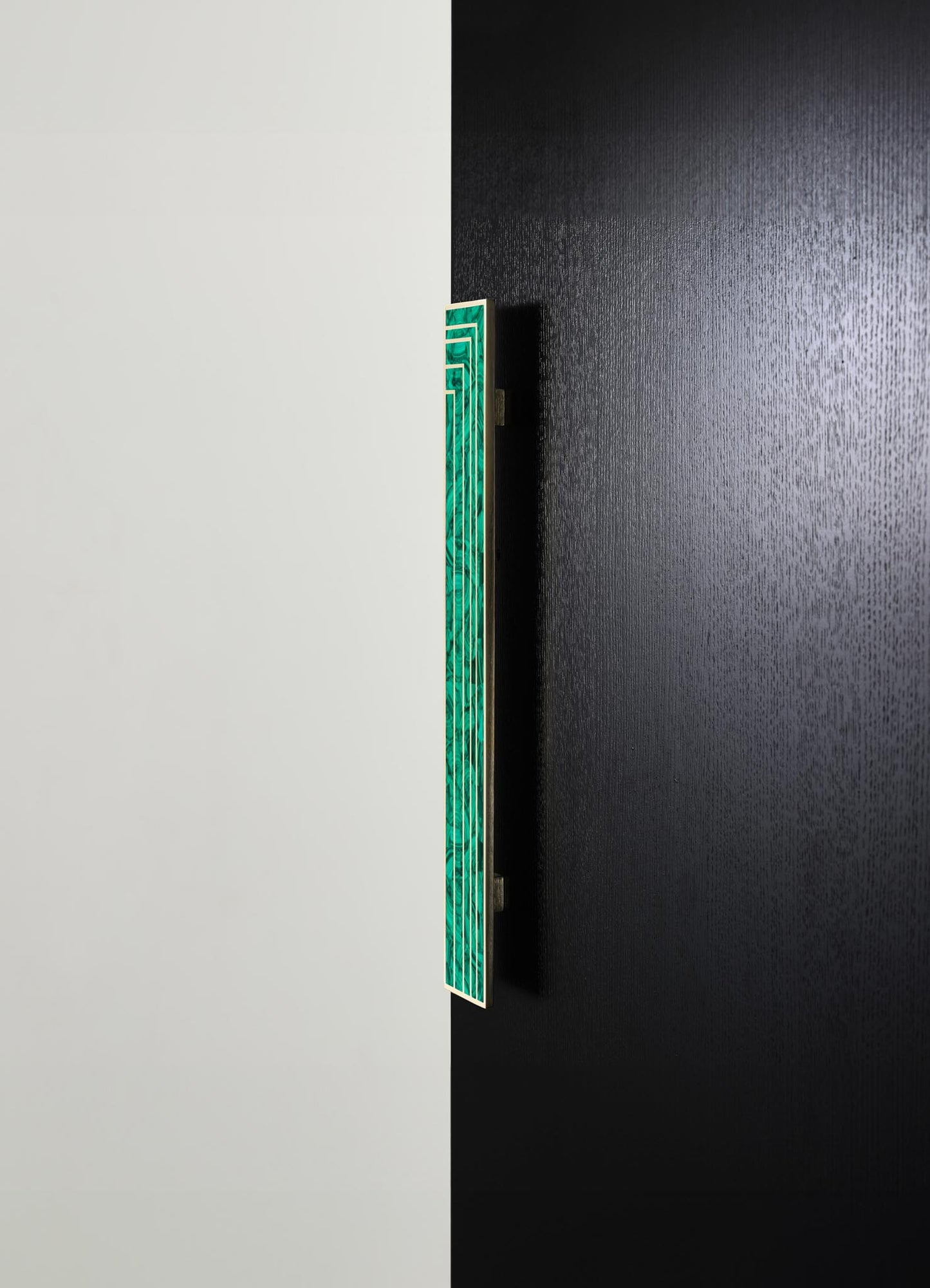 A wall-mounted mirror with a green marble frame featuring geometric patterns, set against a background divided into white and black textured walls.