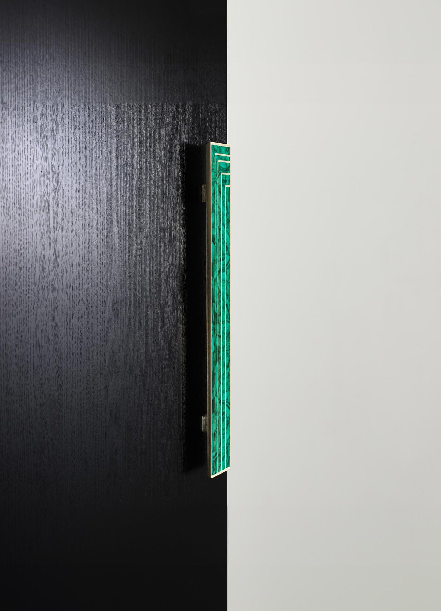 A decorative wall panel featuring green malachite-like inlay with geometric patterns, mounted on a contrasting black and white wall. The panel appears to be made of wood or metal with a glossy finish, exhibiting a contemporary style.