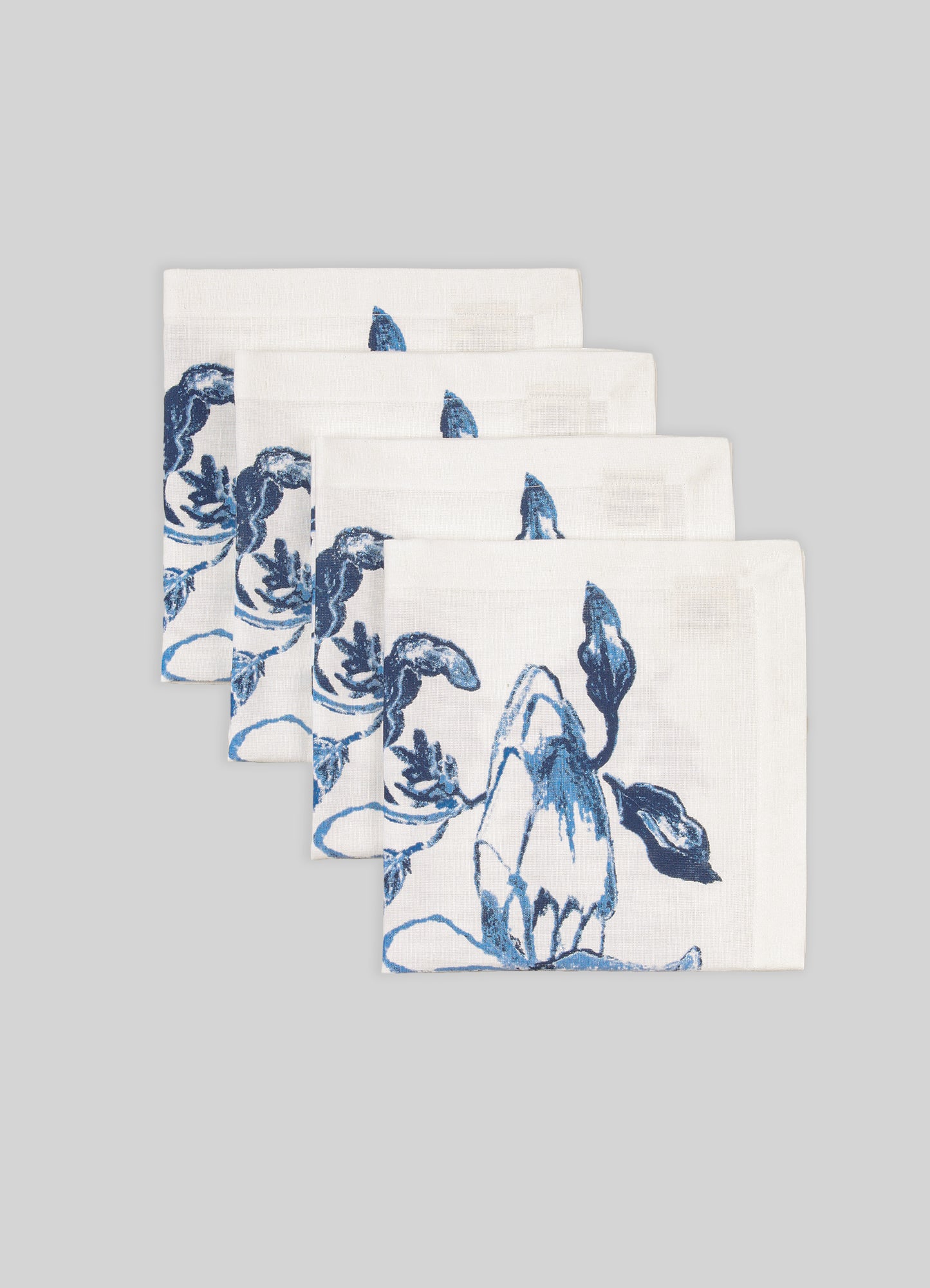 Set of four white napkins with blue floral patterns on a gray background