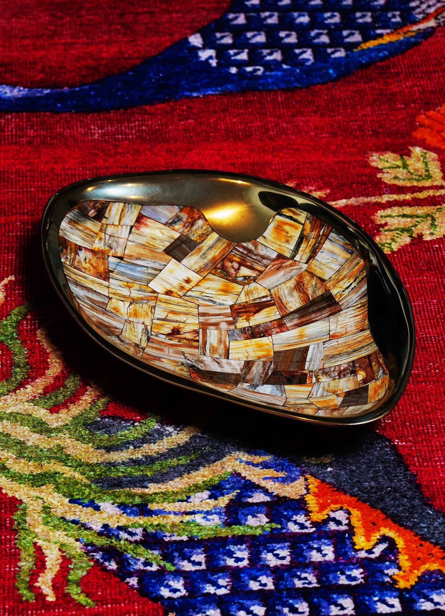 Handcrafted inlaid shell and black lacquer bowl with geometric mosaic pattern, placed on a colorful patterned textile.